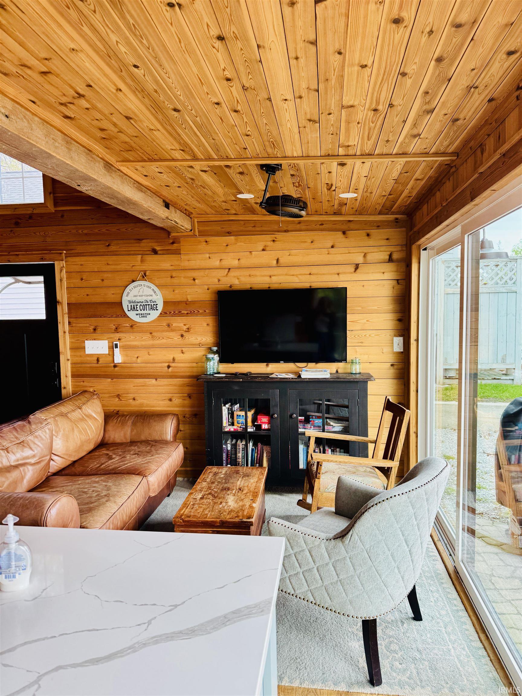Interior space featuring natural wood paneling on walls and ceiling, exposed wood ceiling beam, and large sliding glass doors providing access to an exterior patio with paver flooring