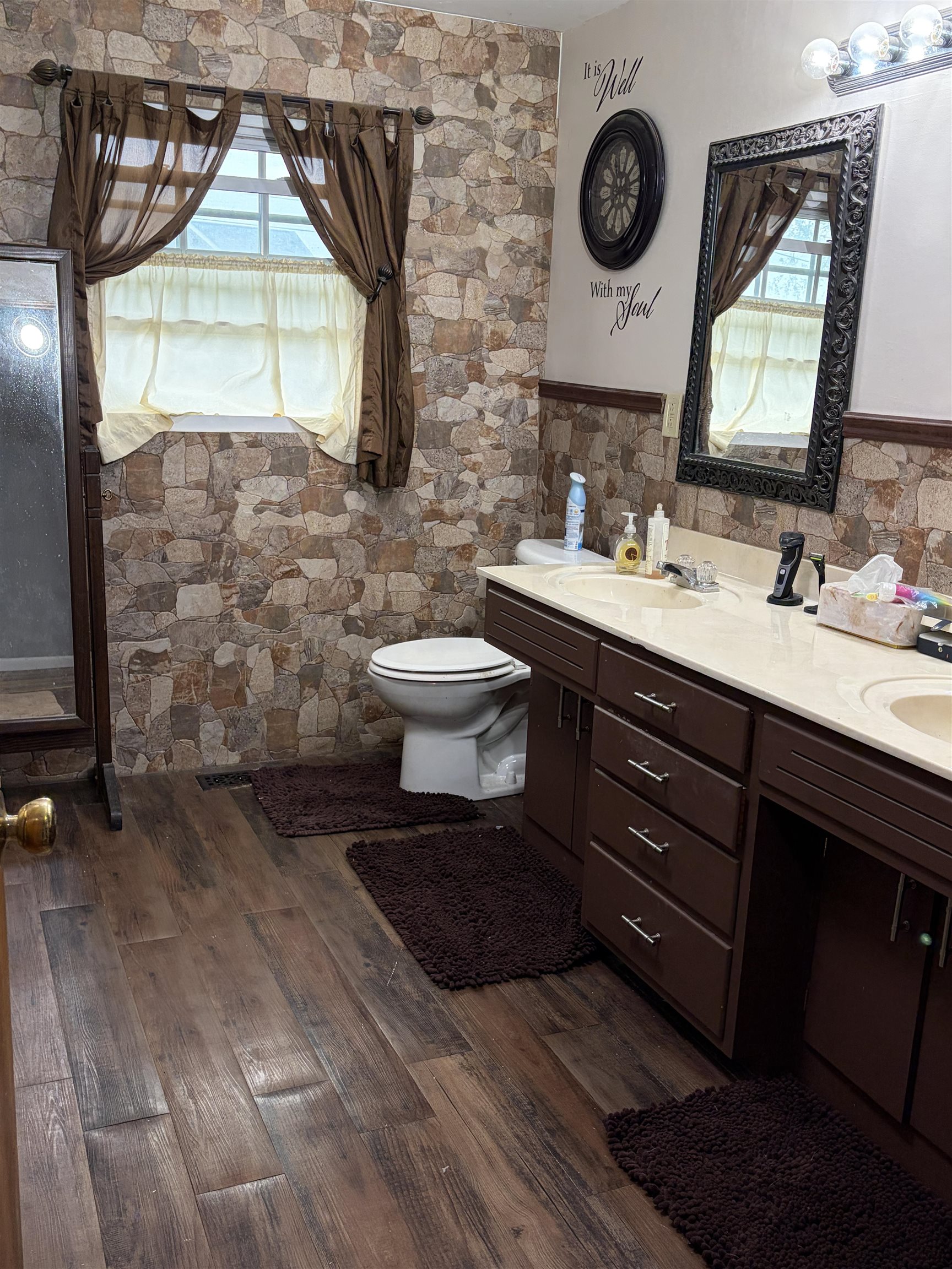 Spacious bathroom featuring wood-finish flooring, a double vanity with light-toned countertops, and rich brown cabinetry