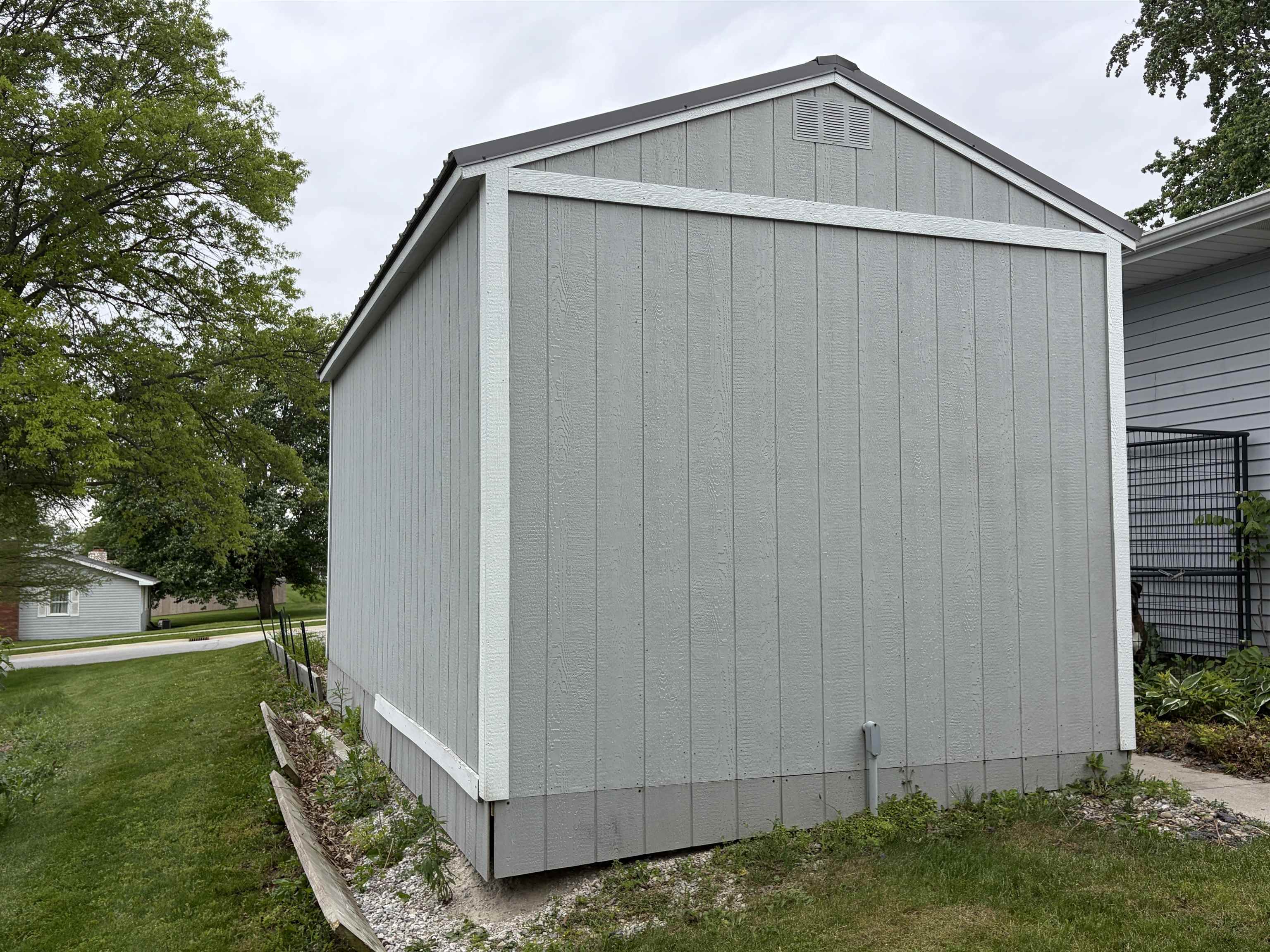 Gable-roofed outbuilding with light gray vertical siding and white trim