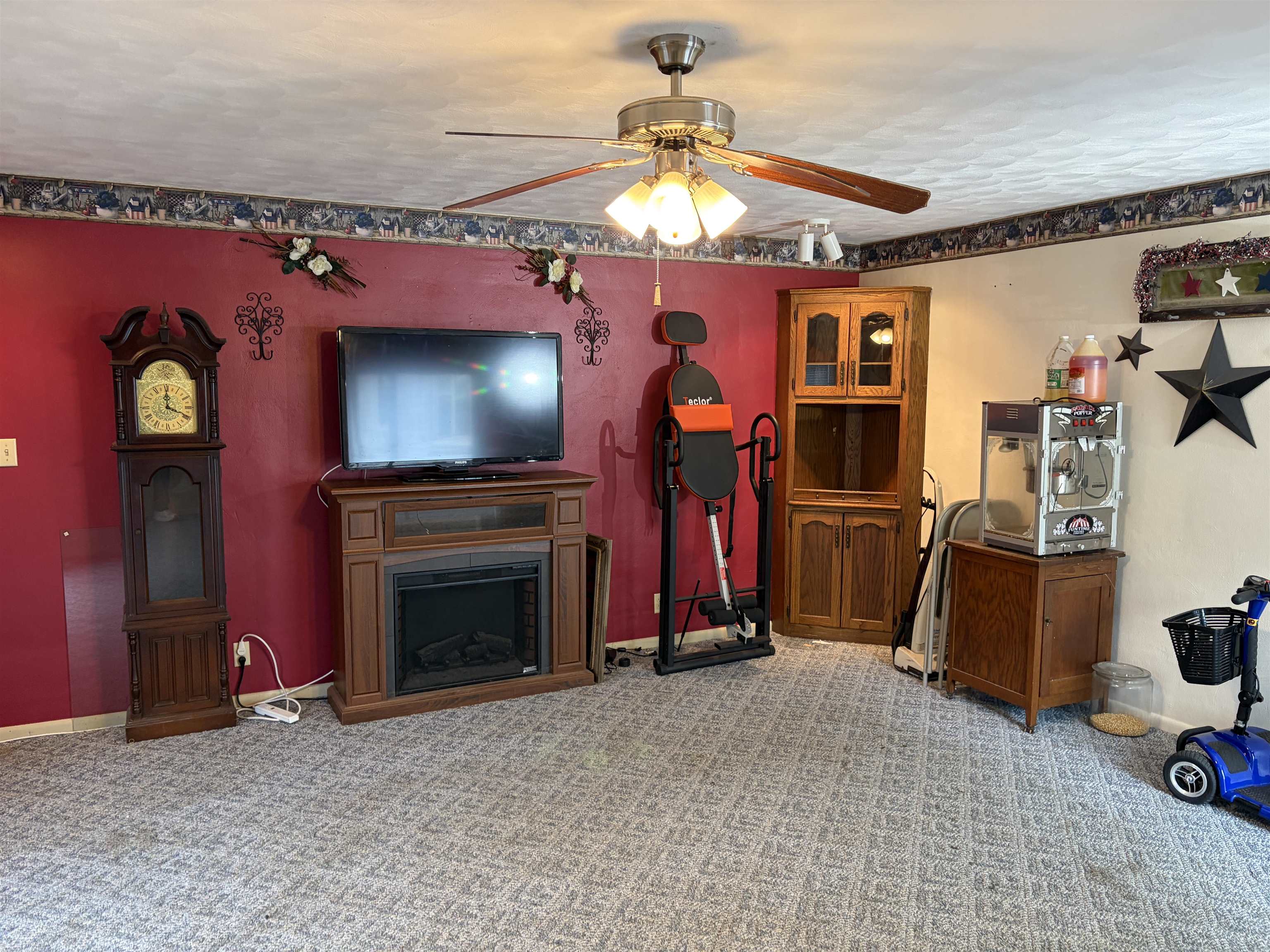 Ceiling fan with light kit, textured ceiling, patterned carpeting, and an electric fireplace with a wood-finish mantel