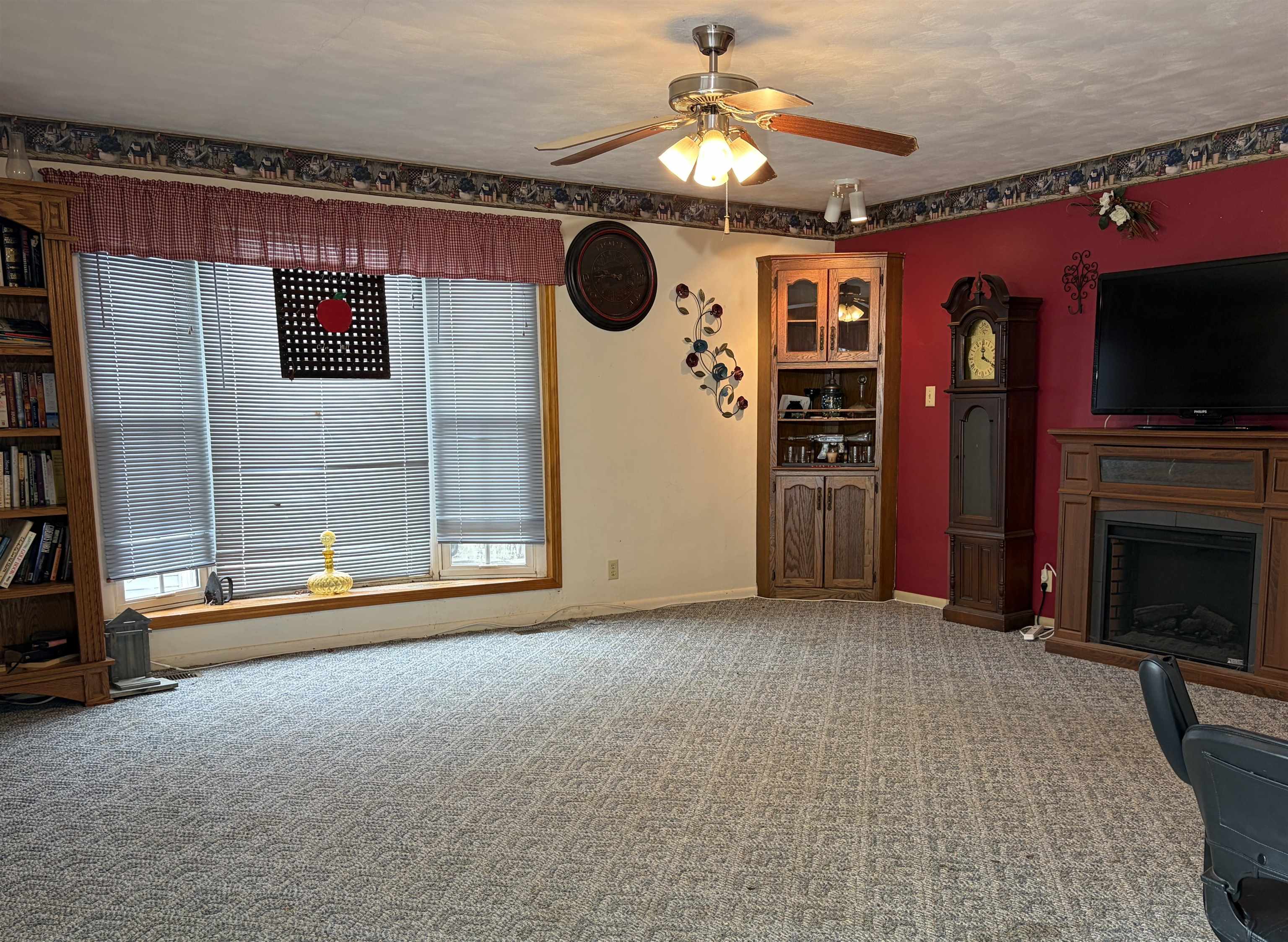 Spacious living area featuring patterned carpet flooring, a ceiling fan with integrated lighting, and a bay window with blinds