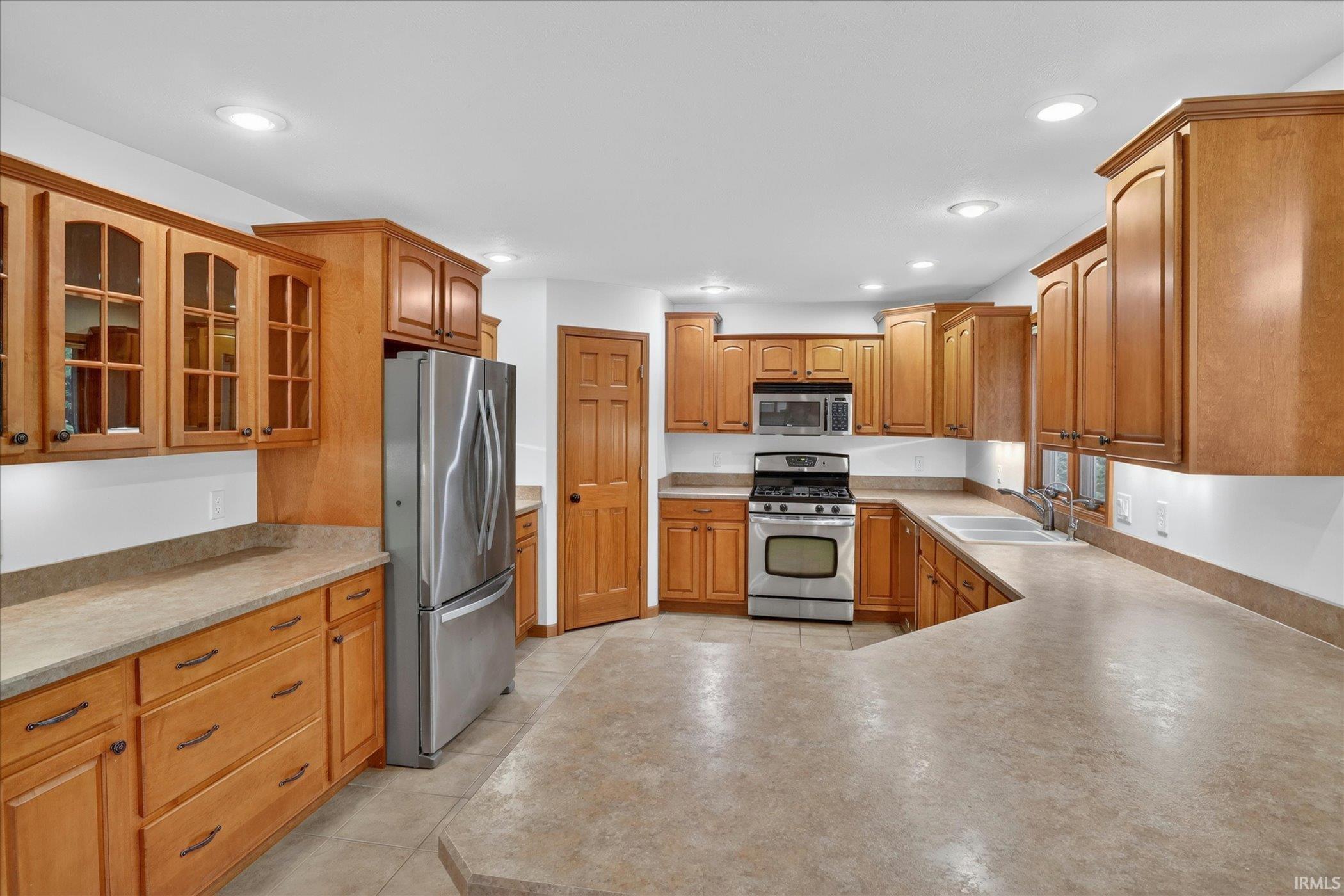 Spacious kitchen featuring a large island, wood-finish cabinetry, stainless steel appliances, recessed lighting, and ample counter space