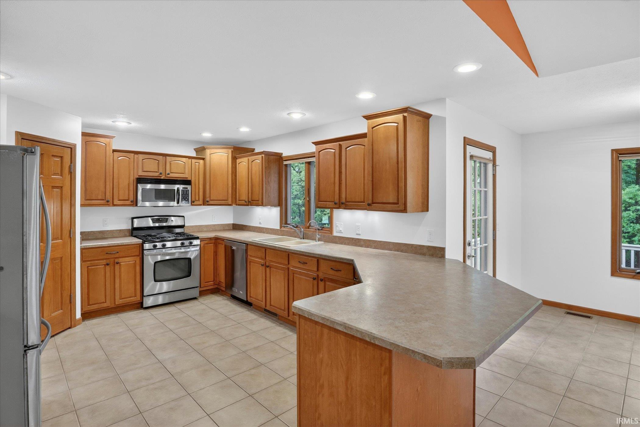 Spacious kitchen featuring extensive wood cabinetry, stainless steel appliances, a breakfast bar, recessed lighting, and tile flooring