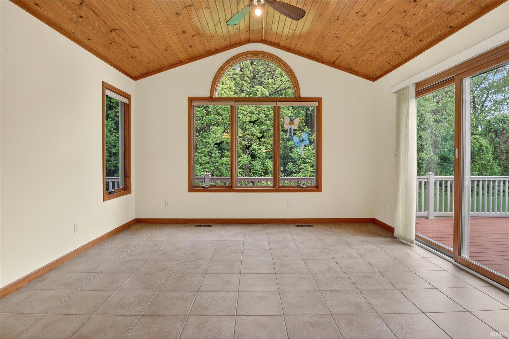 Spacious room with a vaulted wood-plank ceiling, neutral-toned tile flooring, and a large arched window