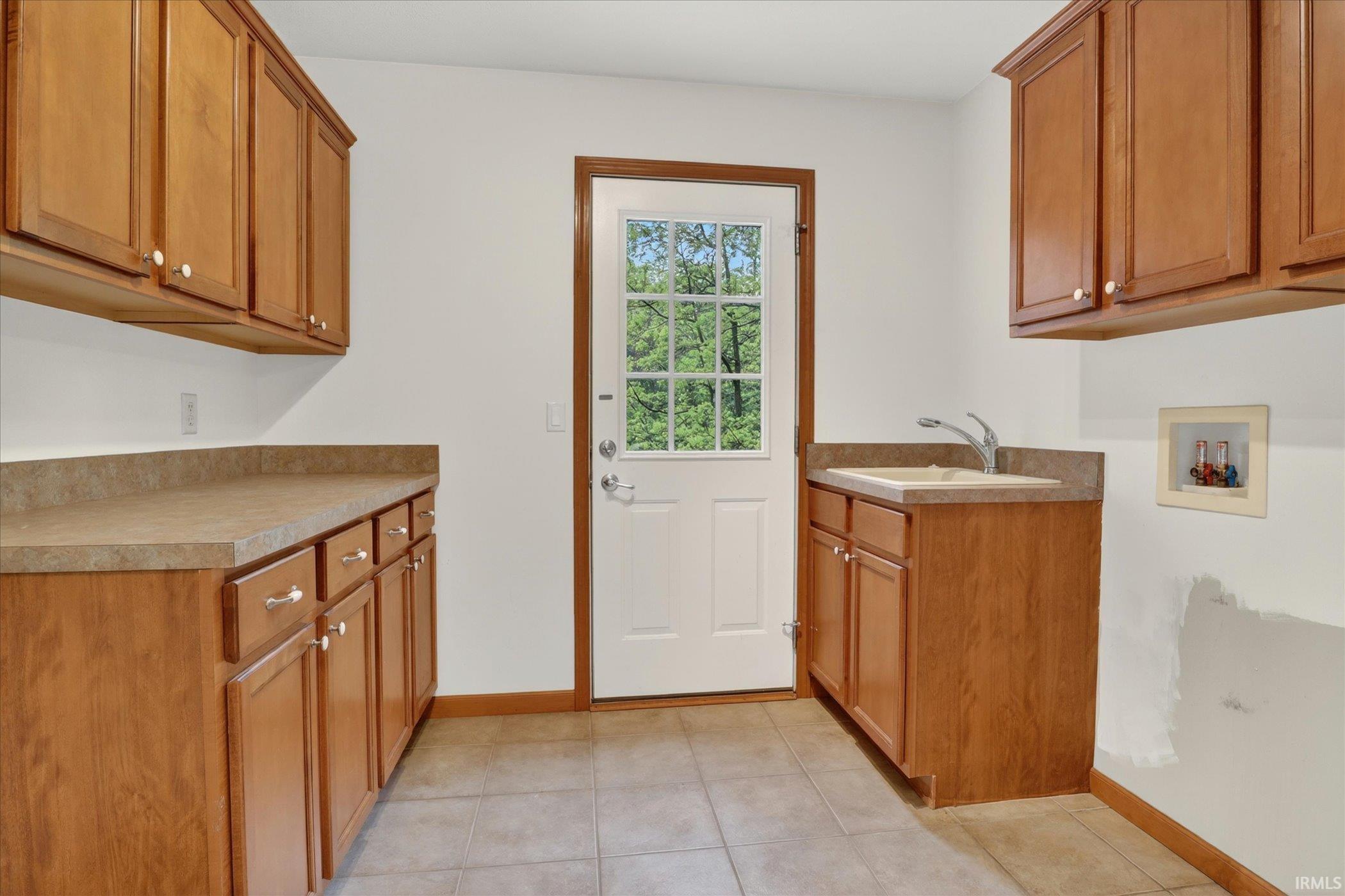 Utility room with wood-finish cabinetry, ample countertop space, a utility sink, and a glass-paneled exterior door