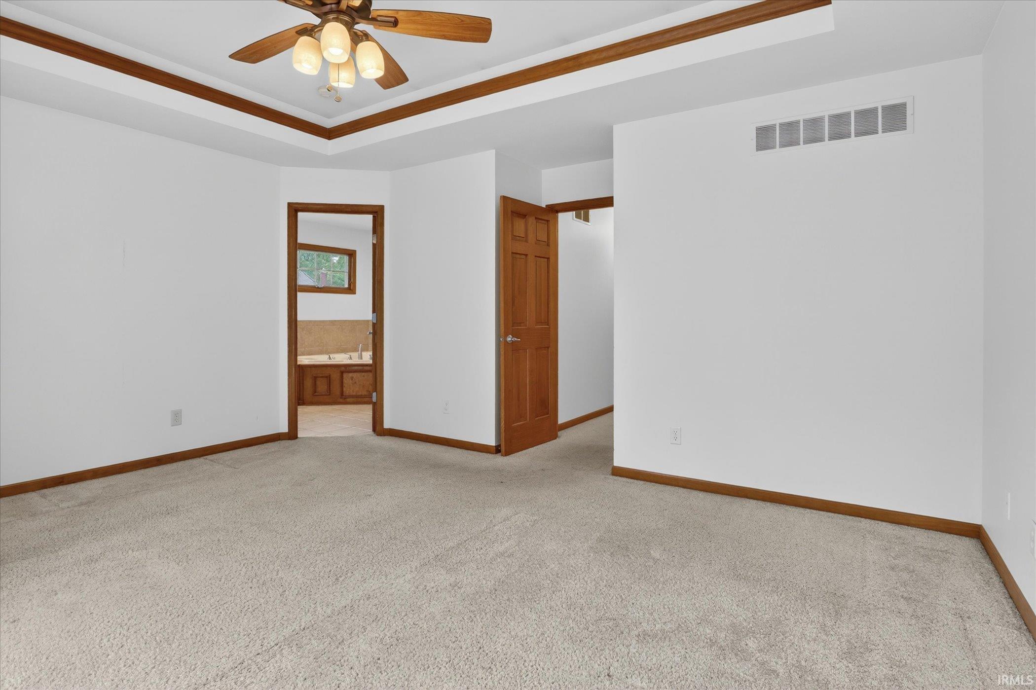 Carpeted interior space featuring a tray ceiling with wood trim, a ceiling fan with integrated lighting, and multiple wood-paneled doors