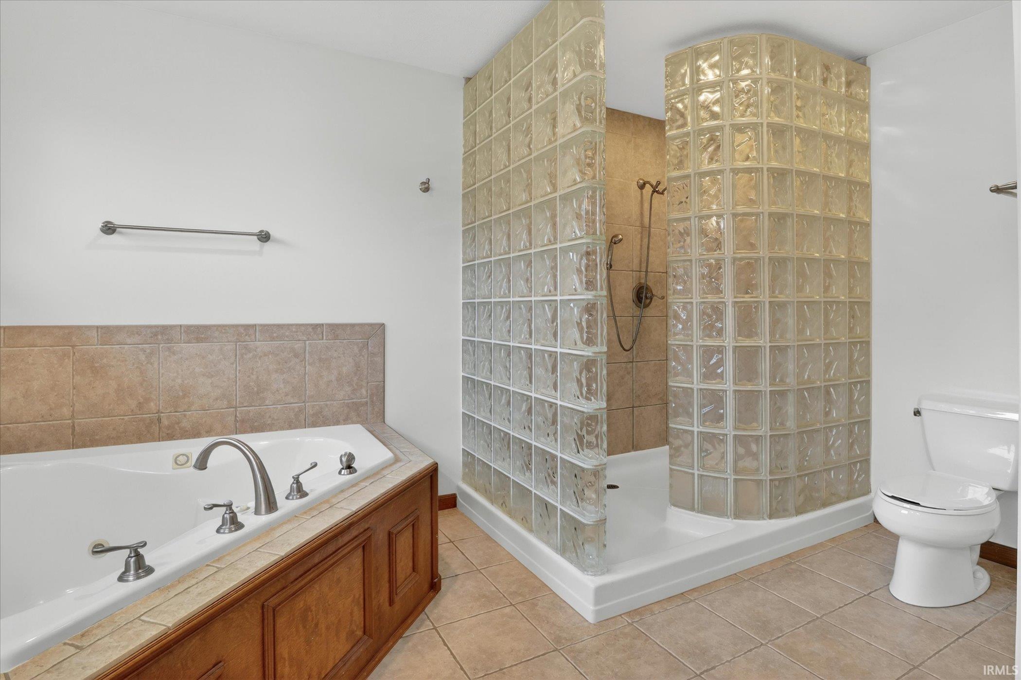 Bathroom featuring a glass block shower enclosure, a white soaking tub with a tiled surround, a built-in wood-paneled tub base, and tiled flooring