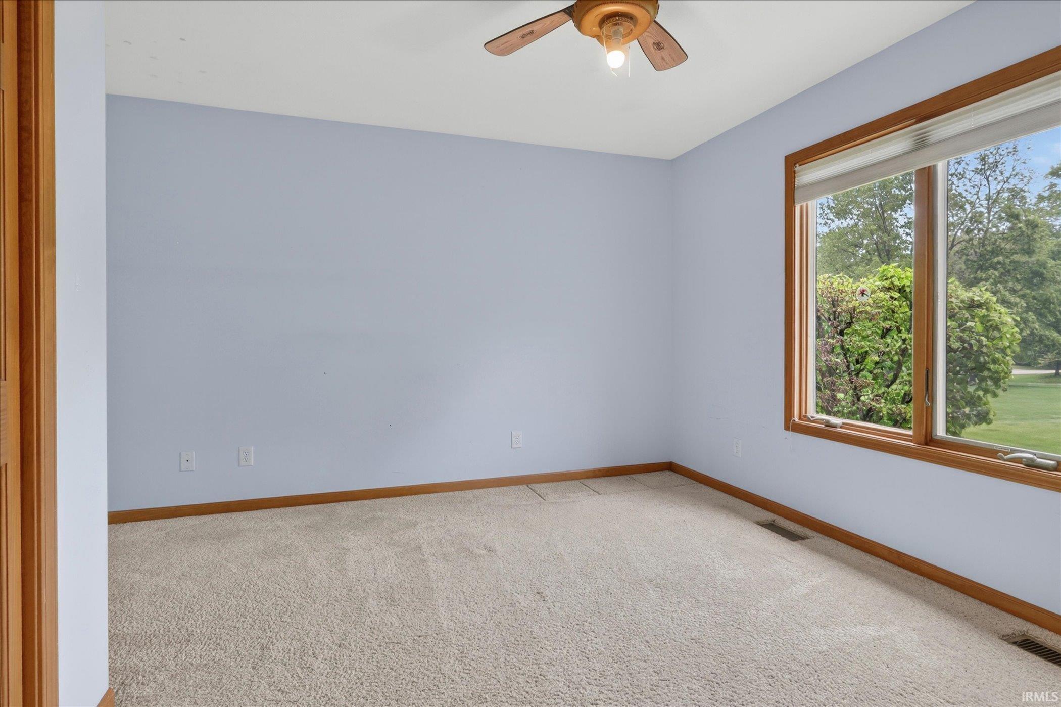 Carpeted room featuring a large window with wood-finish trim, a ceiling fan, light blue walls, and matching wood-finish baseboards