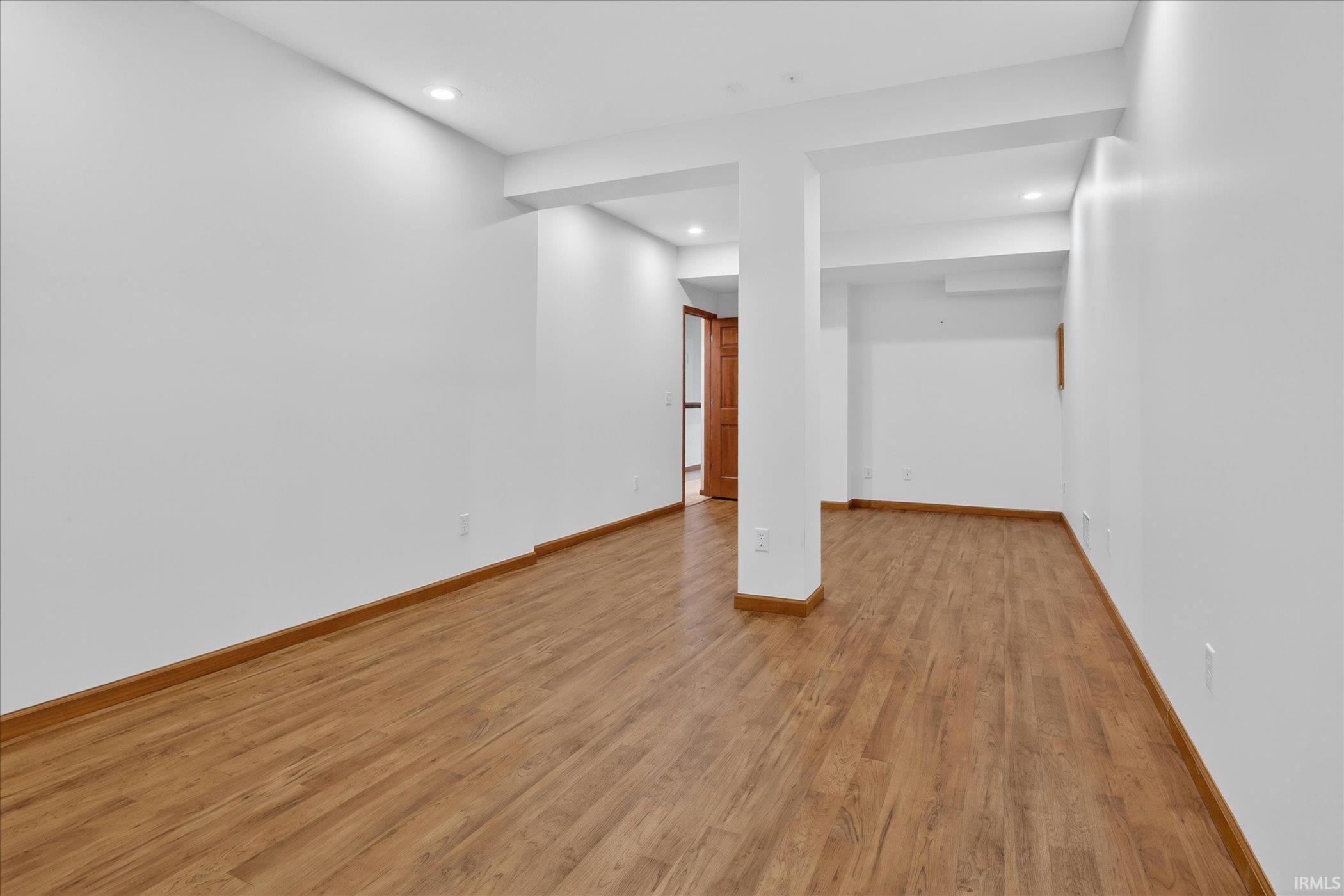 Spacious interior room with wood-finish flooring, recessed lighting, and crisp white walls