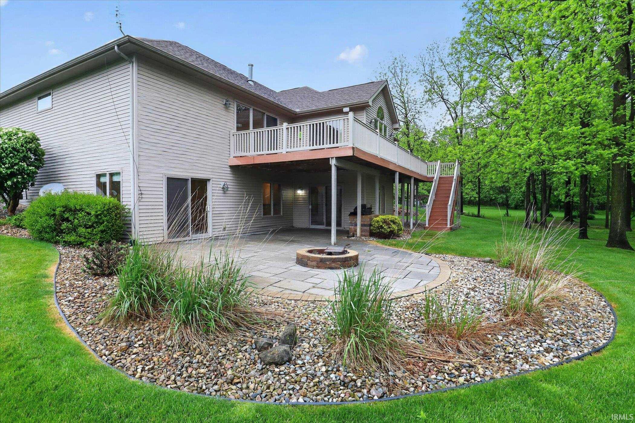 Expansive outdoor living area featuring a multi-level deck with white railings, a lower-level stone patio with a built-in fire pit, and a staircase connecting the upper deck to the yard