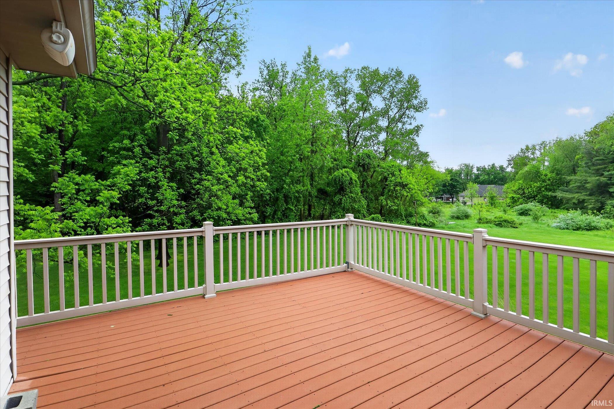 Spacious outdoor deck with brown composite decking and white railing, overlooking a large green lawn and mature trees