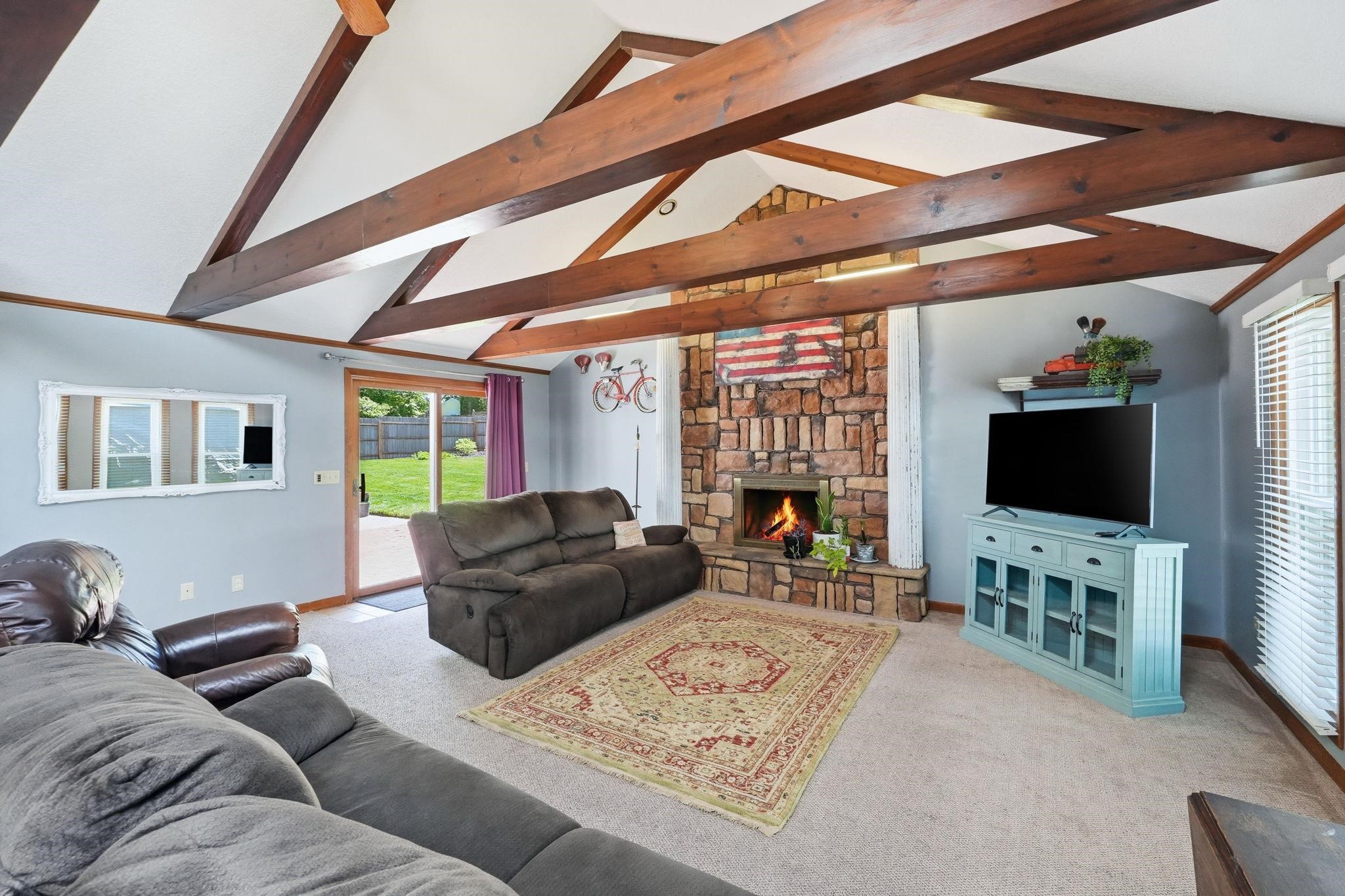 Vaulted ceilings with exposed wood beams, a stone-clad fireplace, and sliding glass doors opening to the backyard