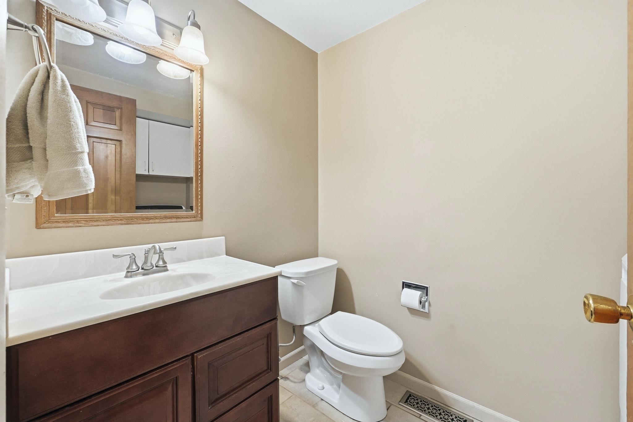 Bathroom featuring a dark wood-finish vanity with a white countertop and integrated sink, a framed mirror, and a three-light fixture