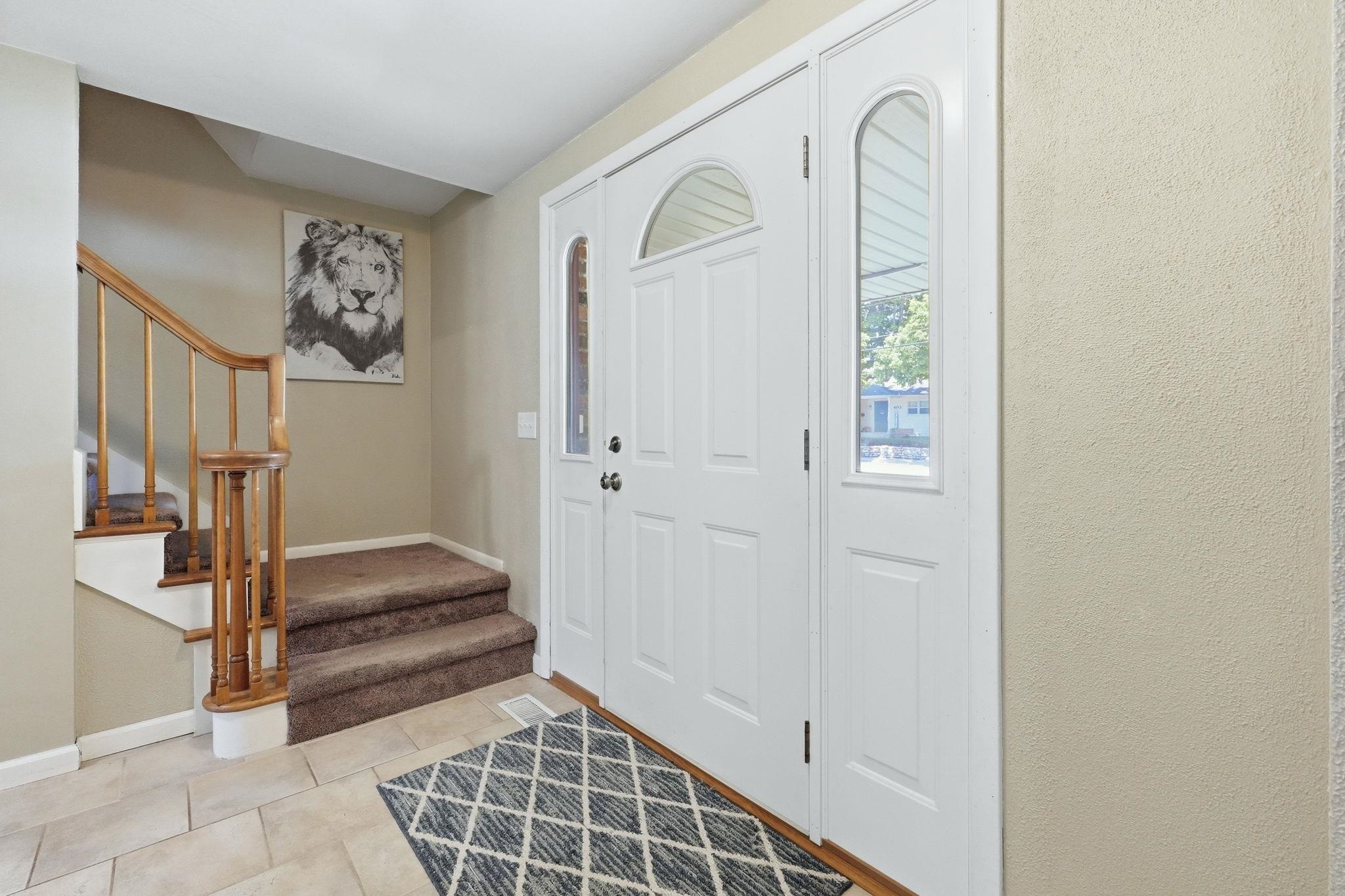 Entryway featuring a white paneled front door with arched transom and sidelight windows, tile flooring, and a staircase with wood railing and carpeted treads
