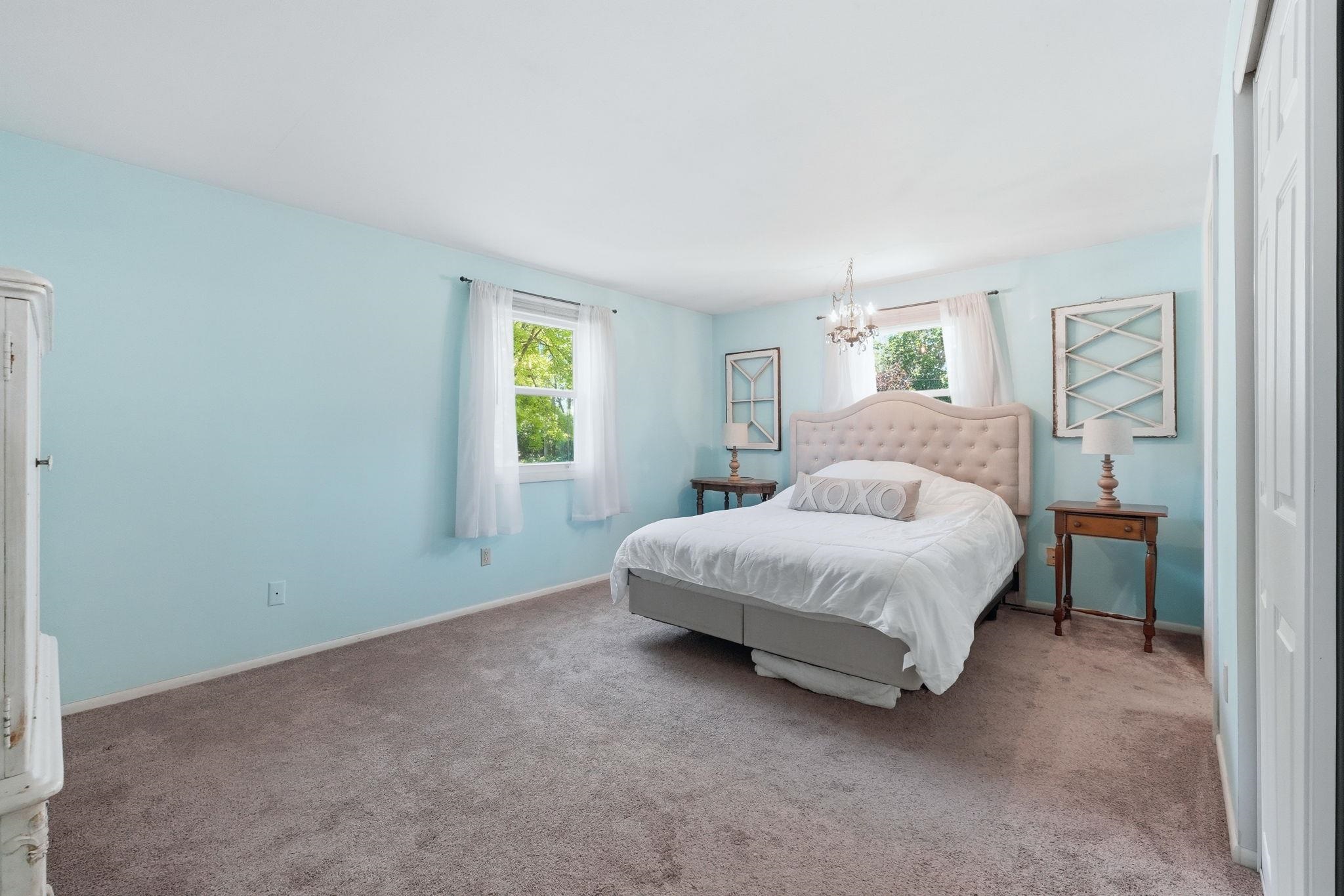 Carpeted room featuring light blue walls, two windows, and a chandelier fixture