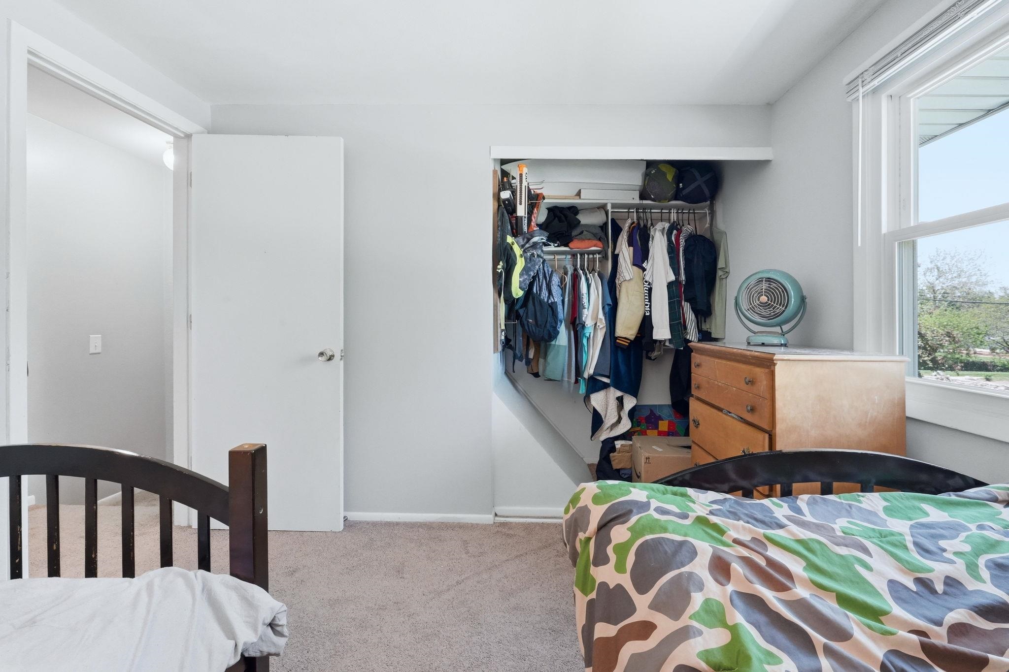 Carpeted interior space featuring a double-hung window, white trim, and a built-in closet with shelving and hanging rods
