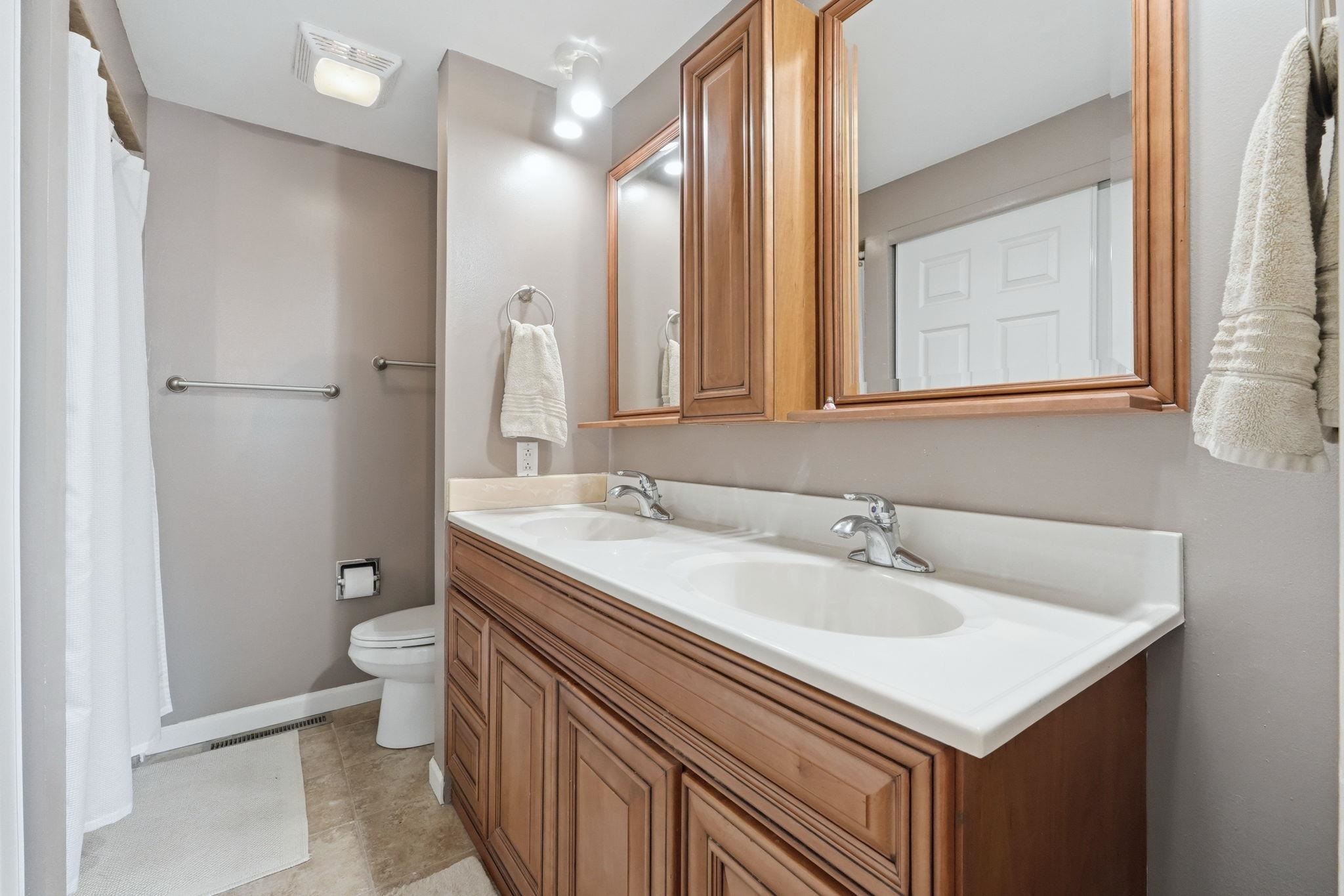 Bathroom featuring a double vanity with light wood cabinetry, dual integrated sinks, and white countertops