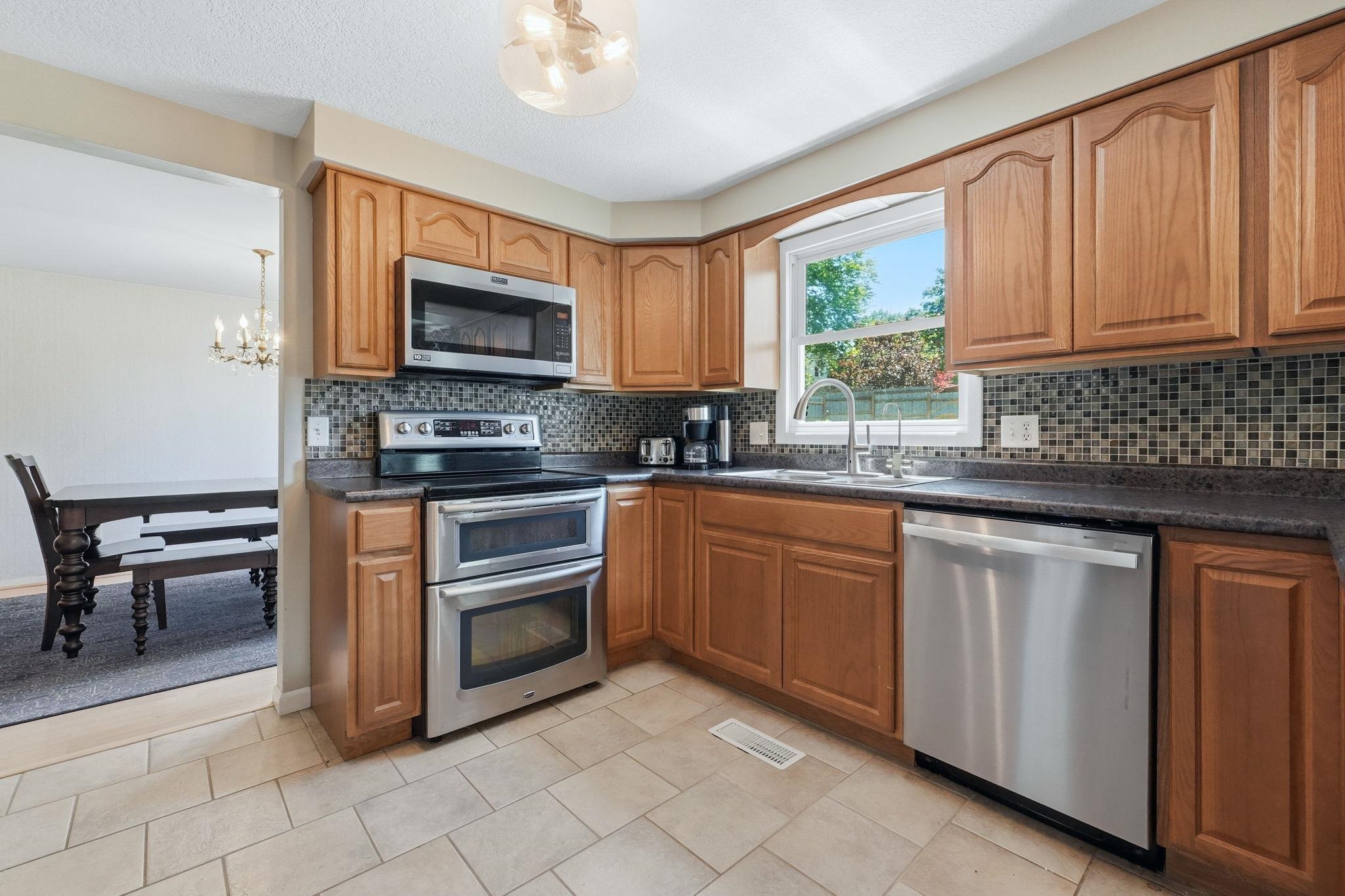 Kitchen featuring wood cabinetry, stainless steel appliances, mosaic tile backsplash, and neutral tile flooring