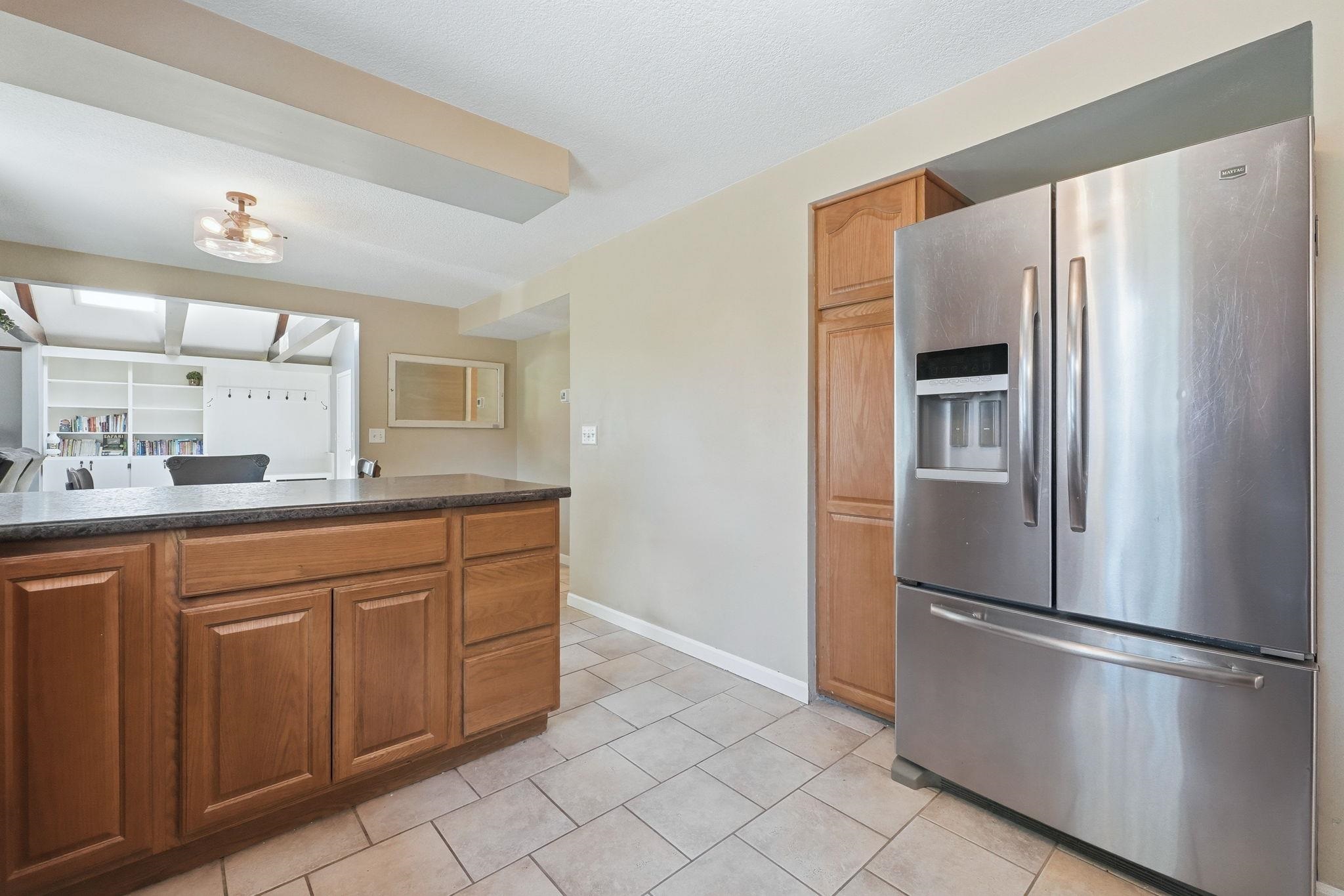 Kitchen featuring a stainless steel French door refrigerator, wood cabinetry, dark countertops, tiled flooring, and an overhead lighting fixture
