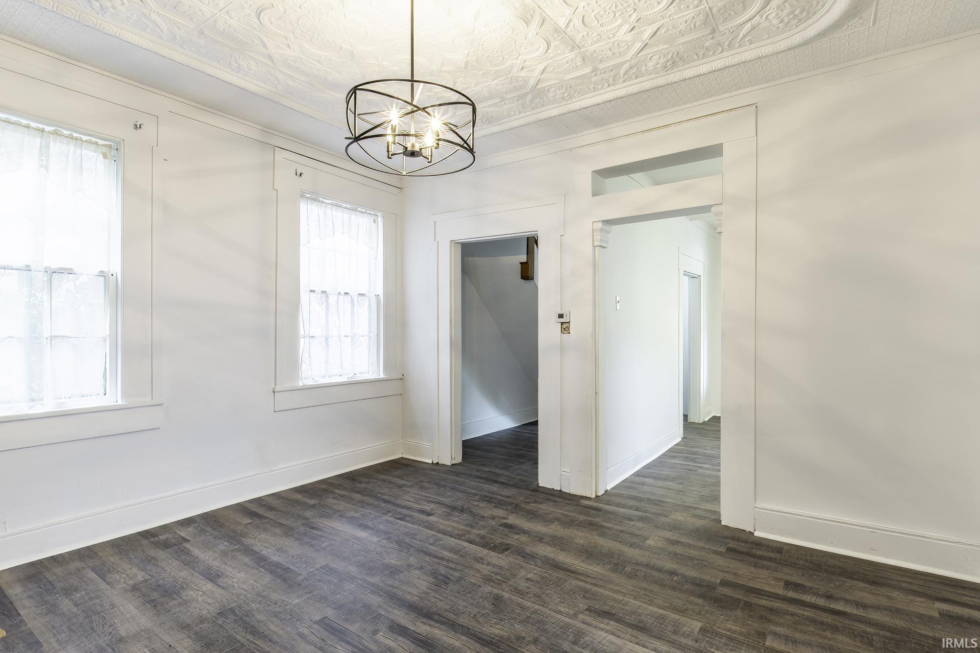 Interior room featuring wood-finish flooring, two windows, a decorative ceiling, and an architectural light fixture