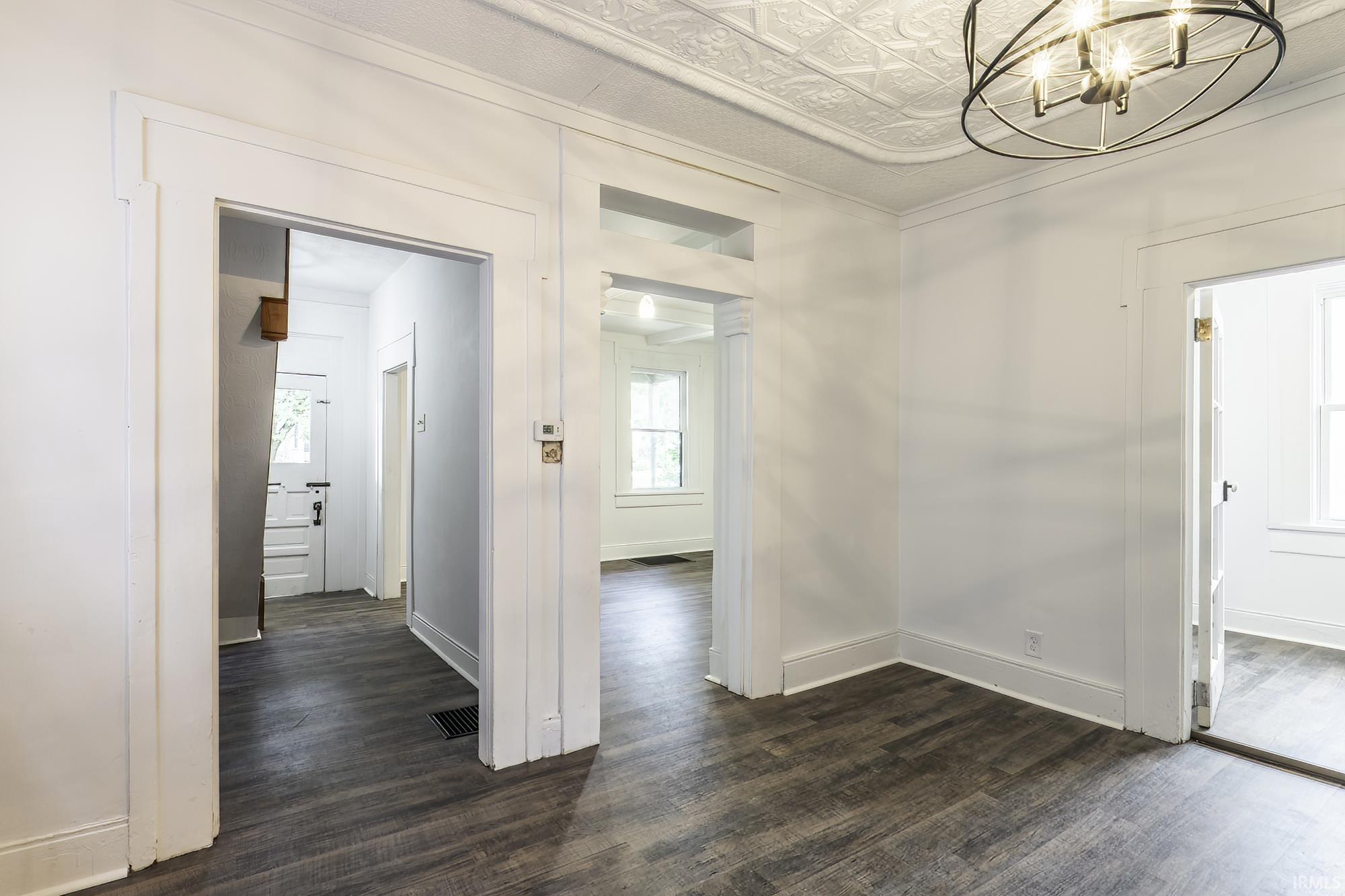 Spacious interior room featuring dark wood-finish flooring, white painted walls, and a decorative pressed tin ceiling