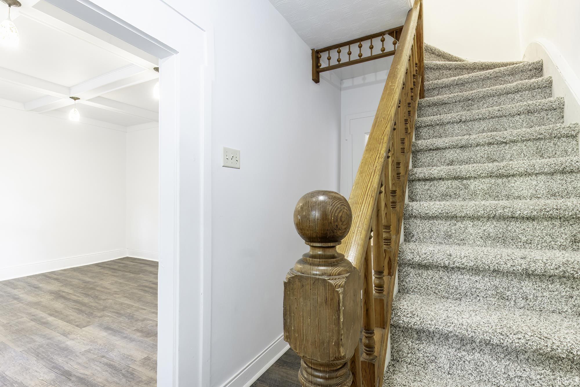Staircase with light gray carpeting and a wood baluster and newel post