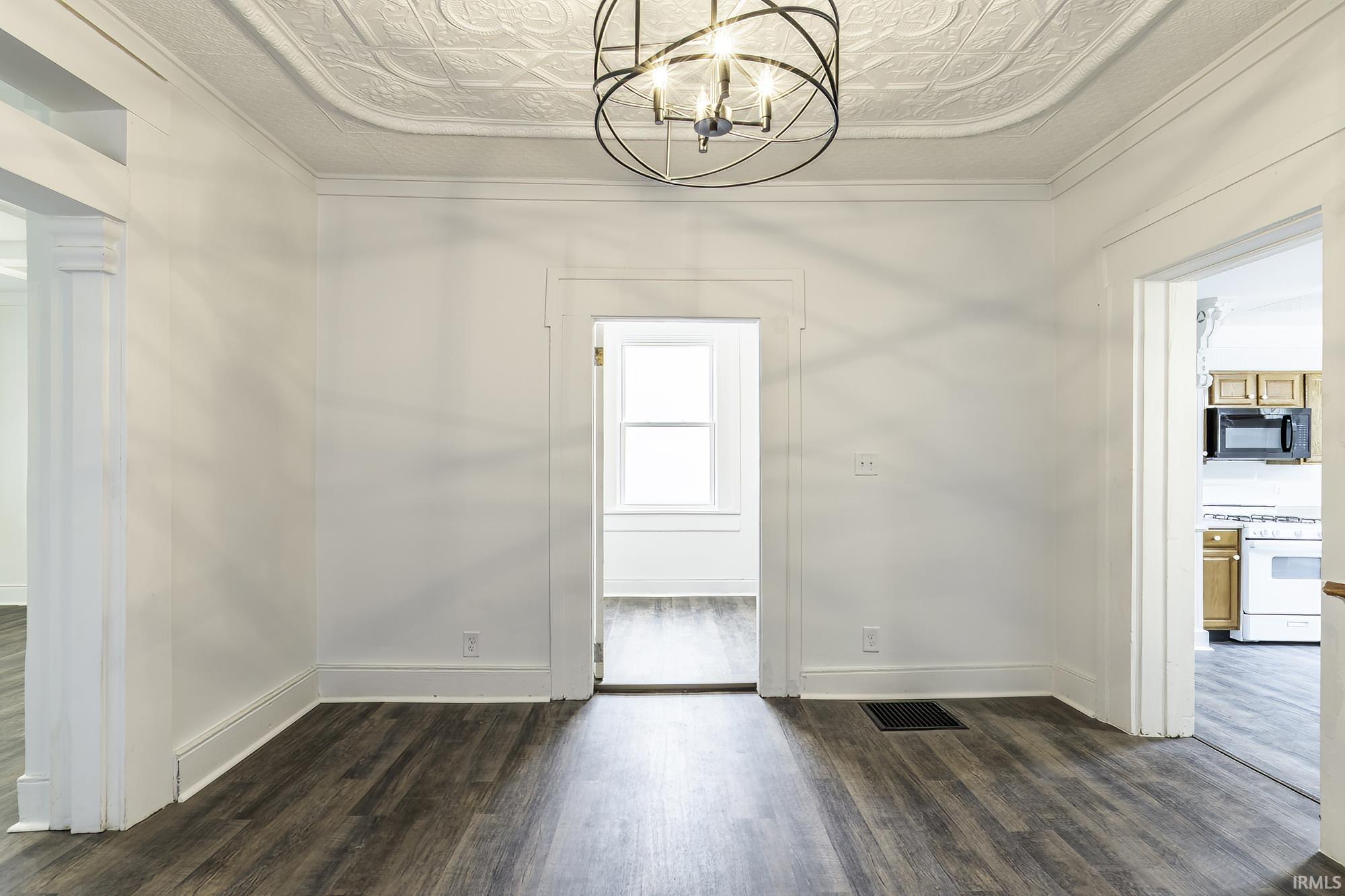 Ornate ceiling featuring a central light fixture, white trim, and wood-finish flooring