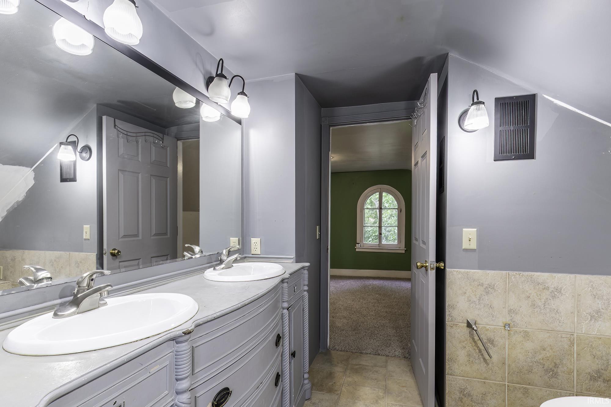 Dual basin vanity with integrated sinks, expansive mirror, and tile flooring