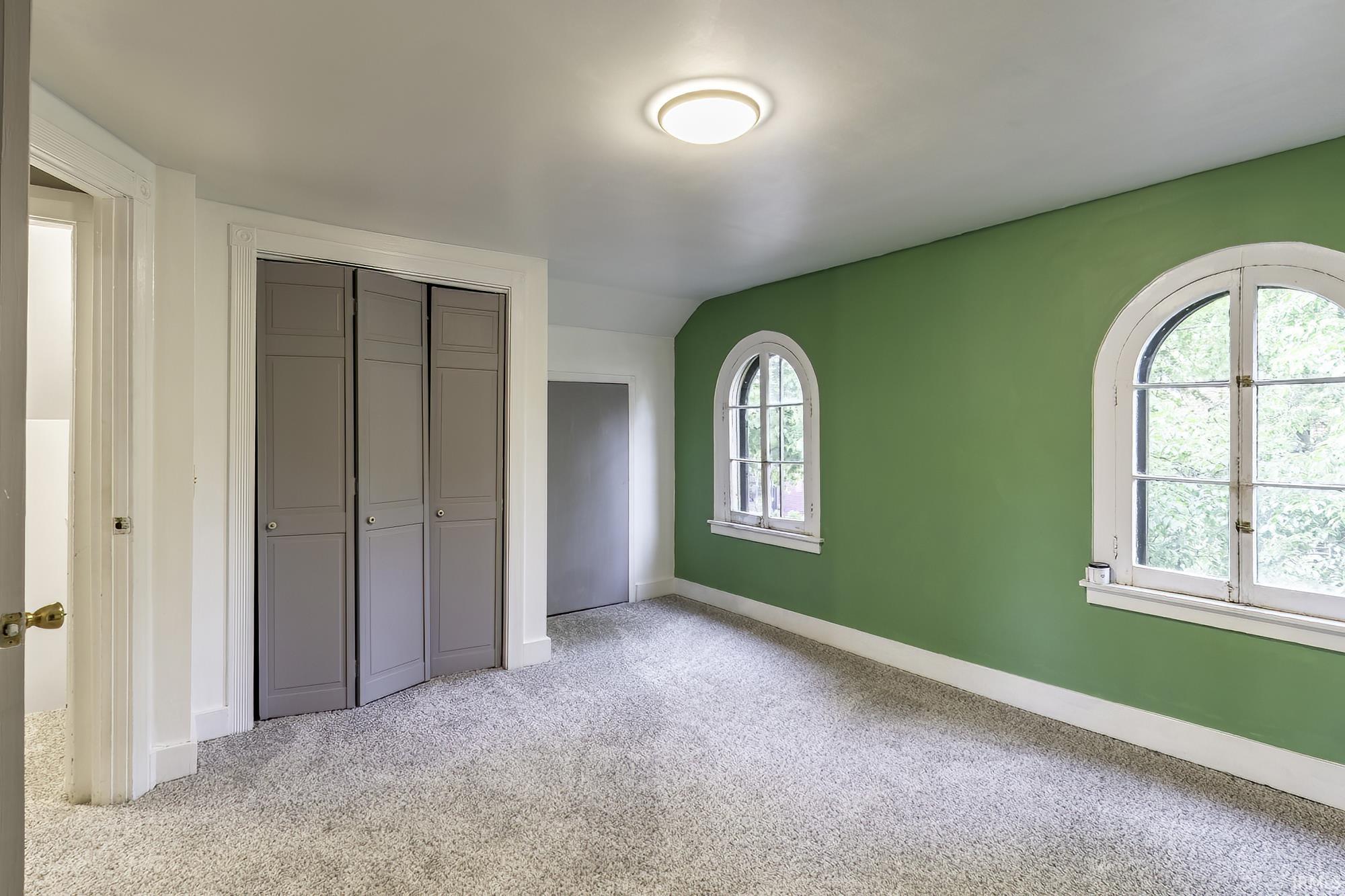 Room featuring two arched windows, light-colored carpeting, and a flush-mount ceiling light