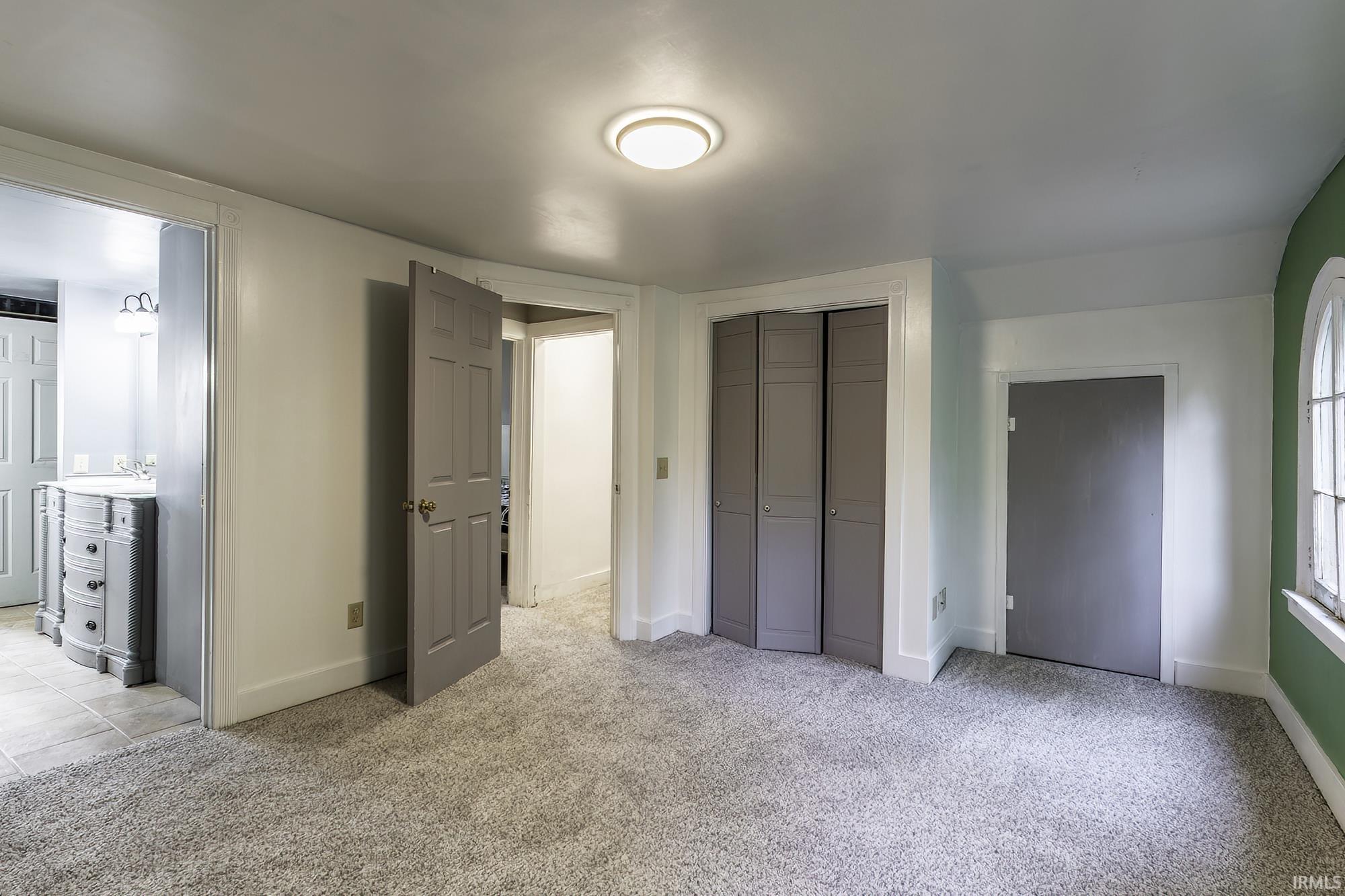 Carpeted room featuring a ceiling-mounted light fixture, multiple panel doors, and an arched window frame