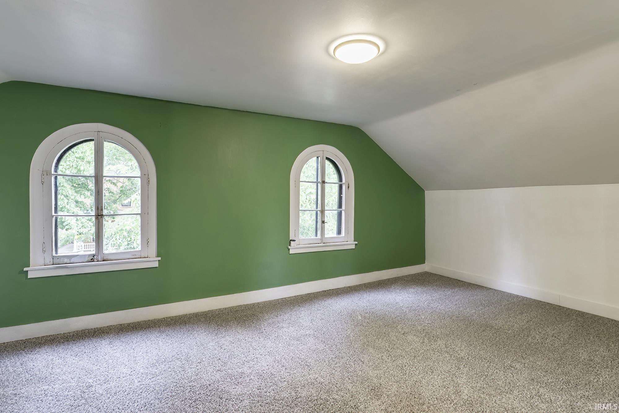Interior space featuring two arched windows, sloped ceilings, wall-to-wall carpeting, and a flush-mount ceiling light fixture