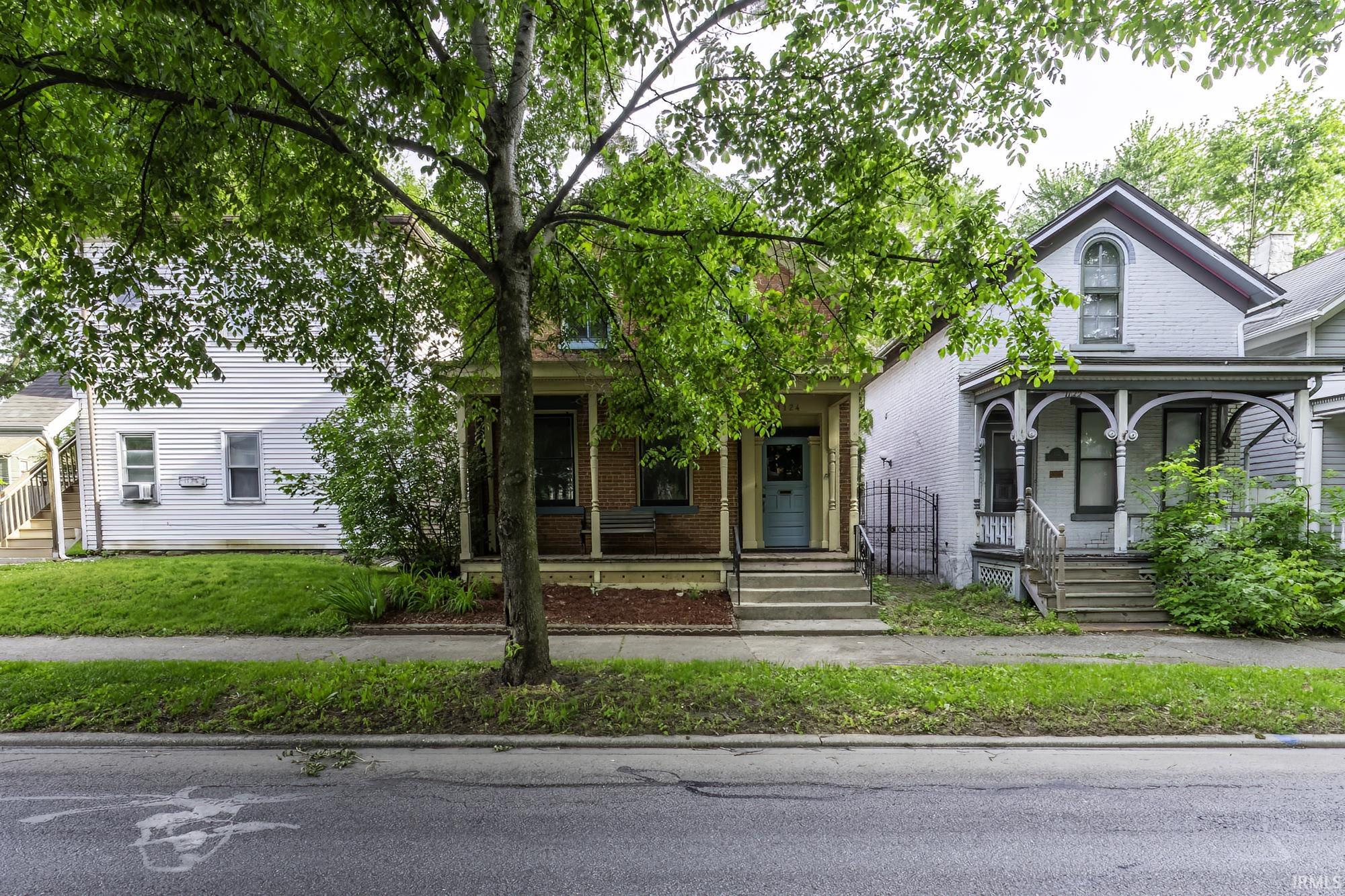 Brick facade residence with a light blue entry door, covered porch, and mature trees