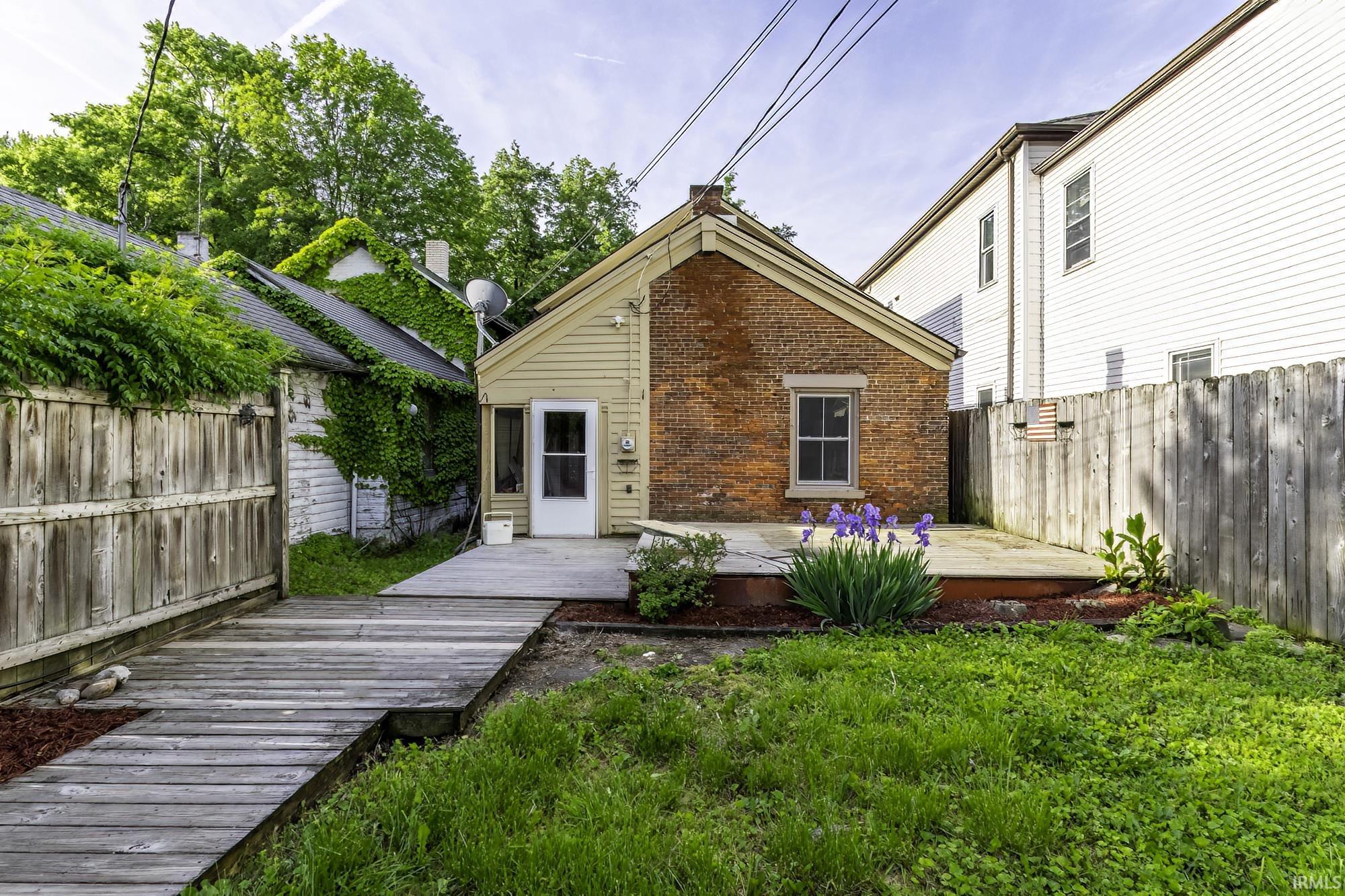 Rear exterior featuring a brick facade with siding, a wooden deck, and an expansive lawn