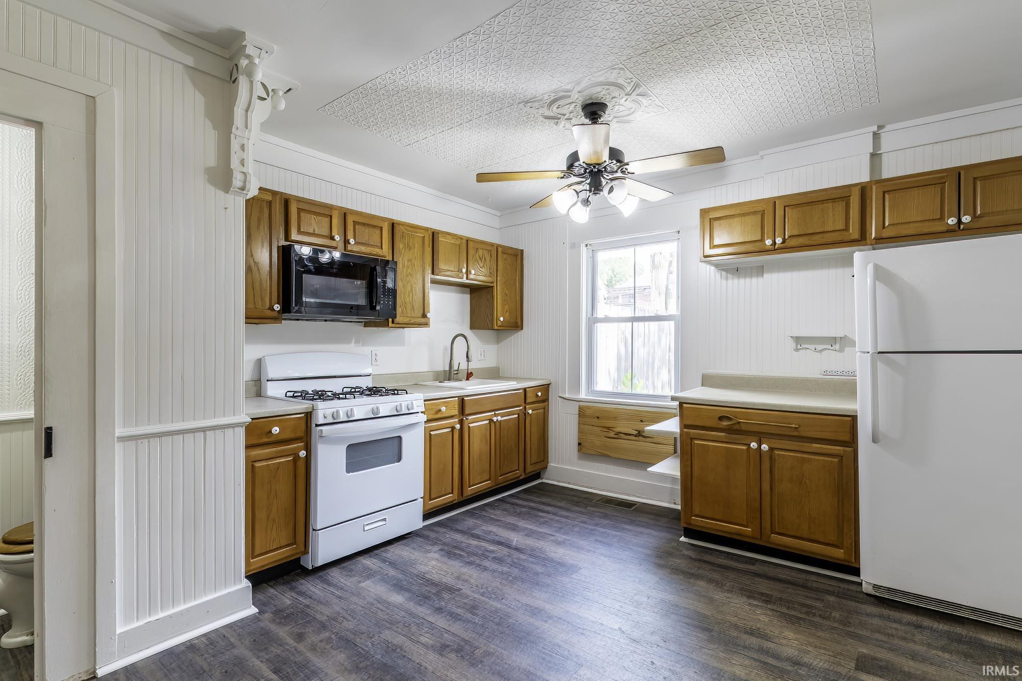 Functional kitchen featuring wood-finish flooring, beadboard walls, and a pressed tin ceiling