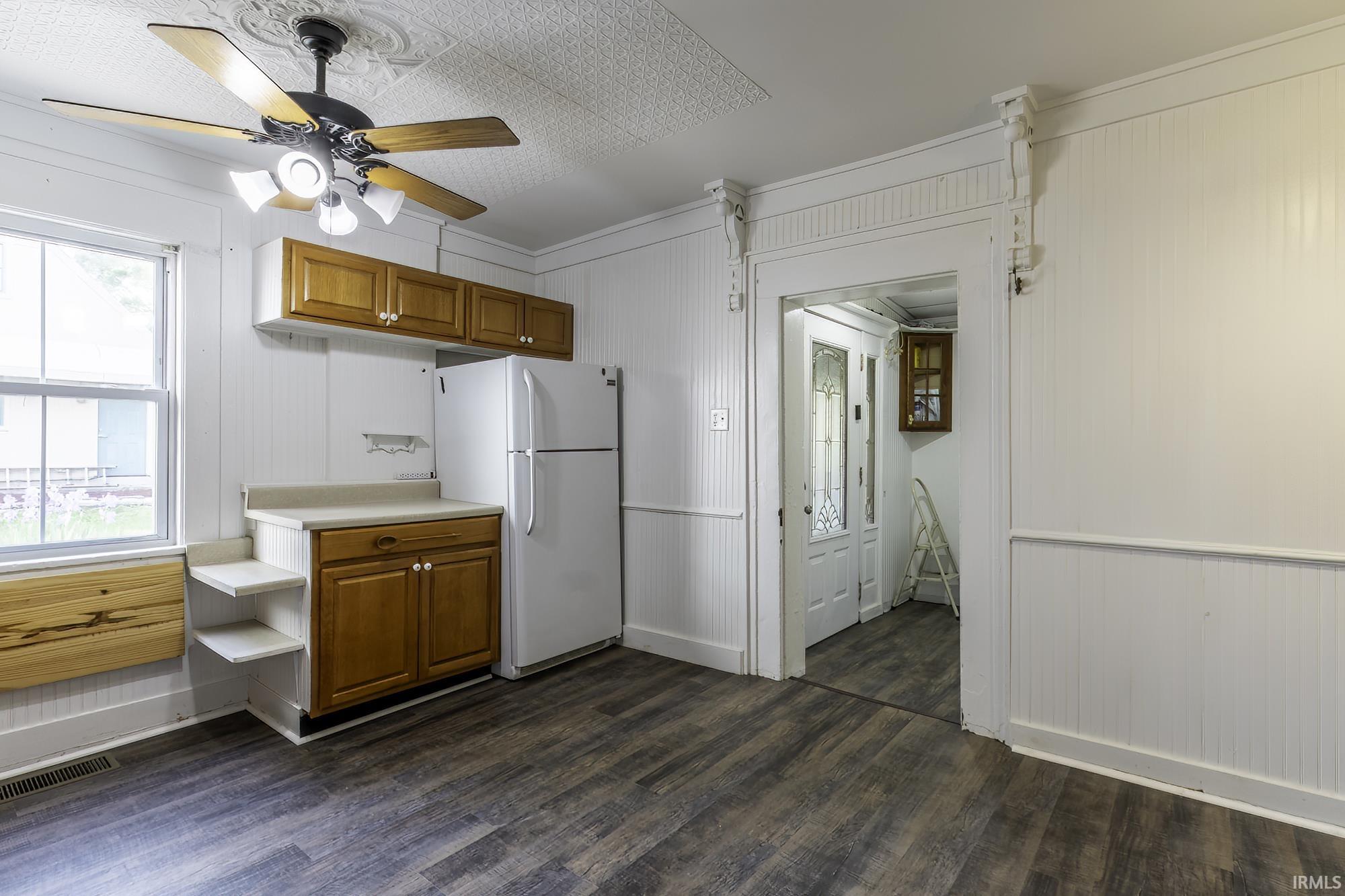 Kitchen area featuring wood-finish flooring, white paneled walls, and a ceiling fan with integrated lighting