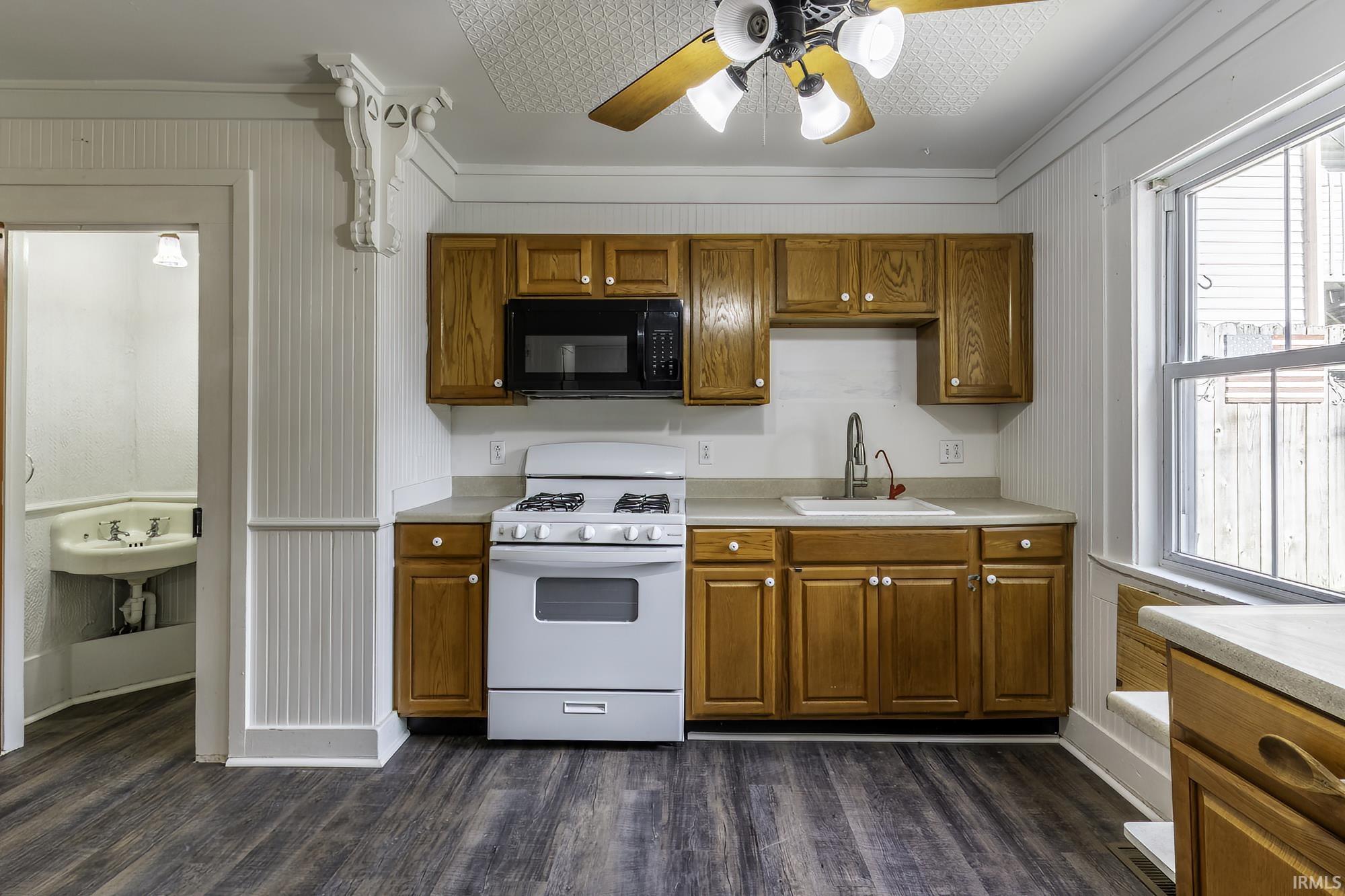 Kitchen featuring wood-finish flooring, wood cabinetry with white hardware, light-toned countertops, and a white gas range with a black microwave