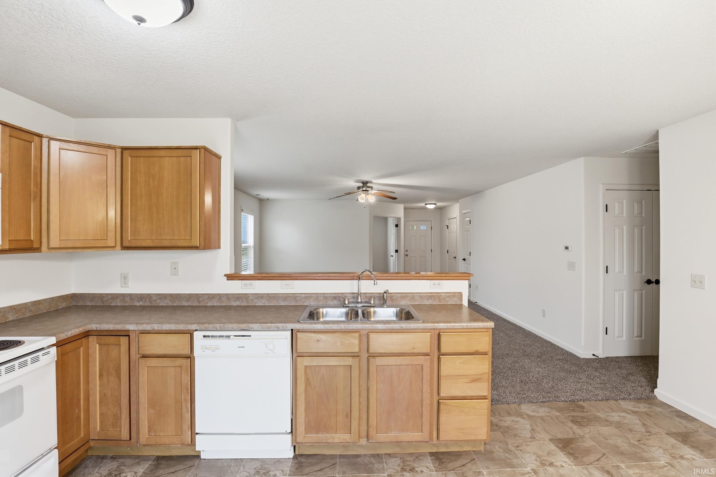 Kitchen featuring wood cabinetry, laminate countertops, a double basin sink, and a white dishwasher
