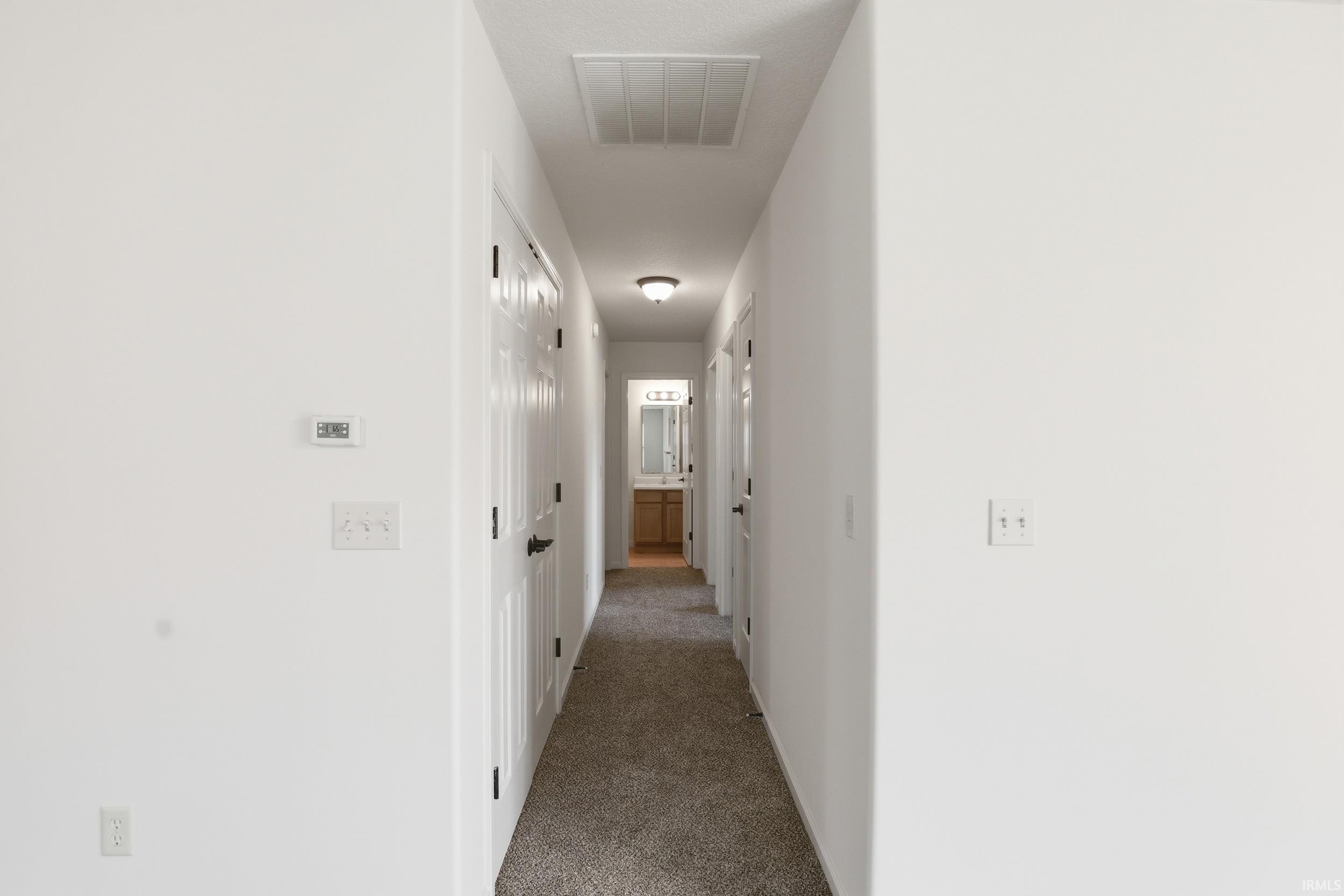 Hallway with light gray carpeting, white walls, and dark hardware on interior doors