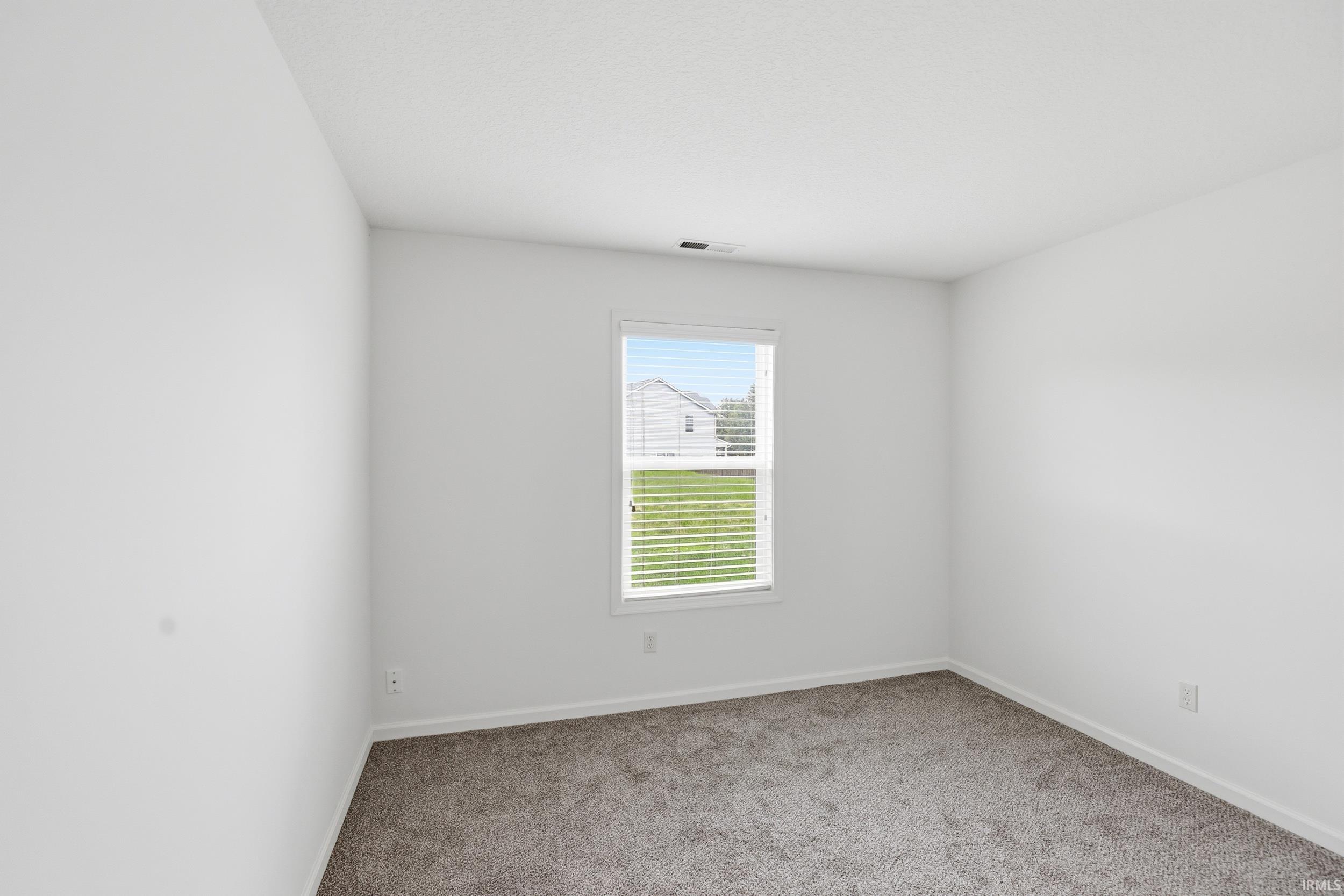 Neutral interior room featuring a window with white blinds, light-colored walls, and gray carpet flooring