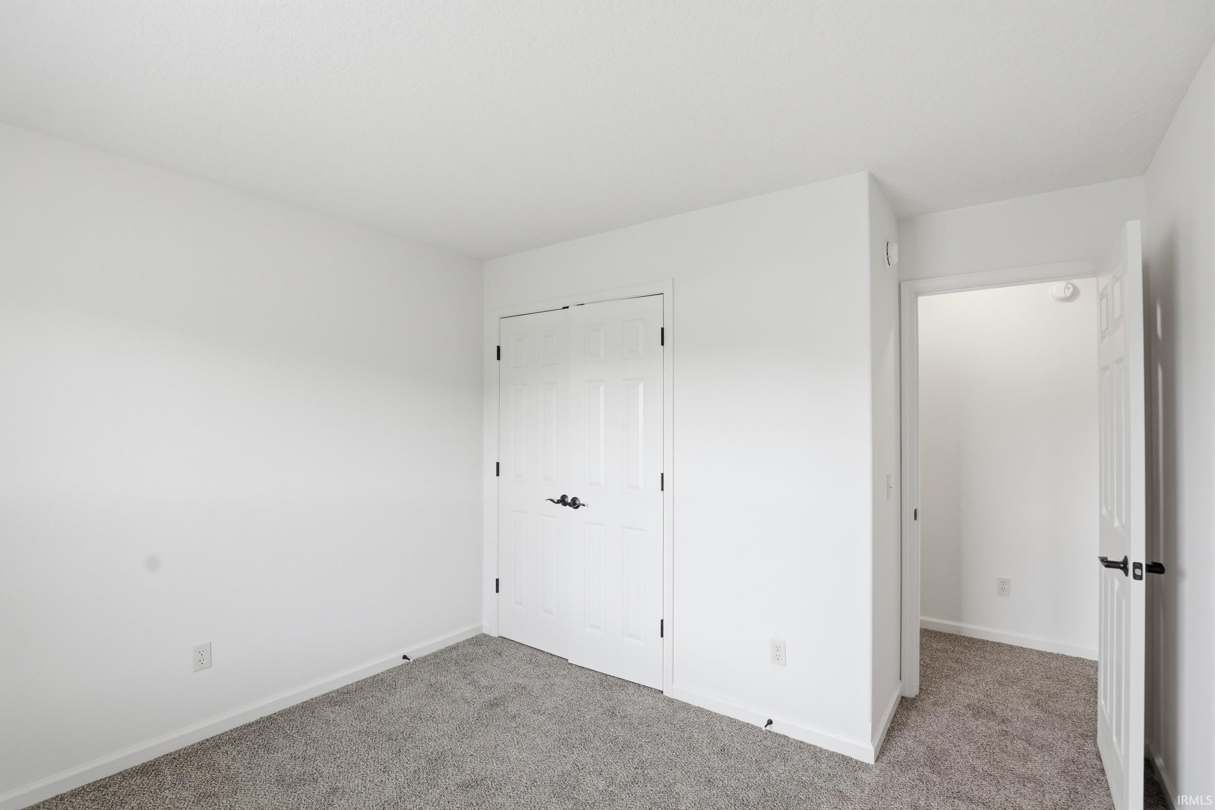 White interior walls, gray carpeting, white baseboards, and white paneled doors with black hardware