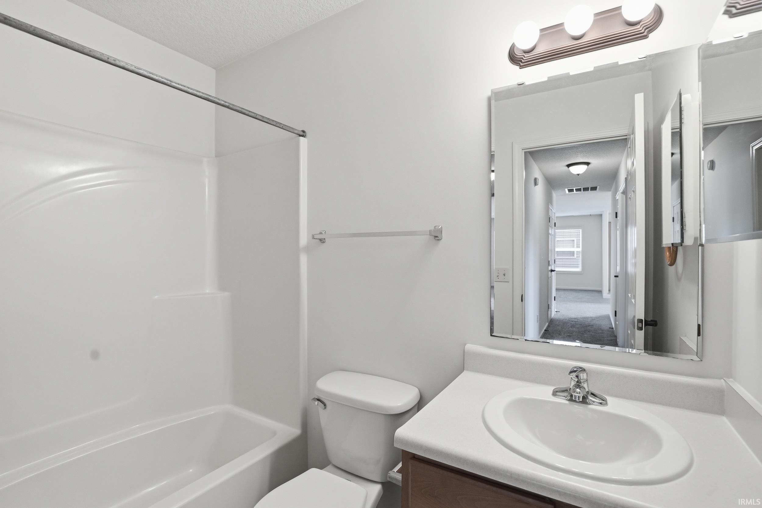 Bathroom featuring a white bathtub with an integrated shower surround, a white toilet, and a vanity with a white countertop and undermount sink