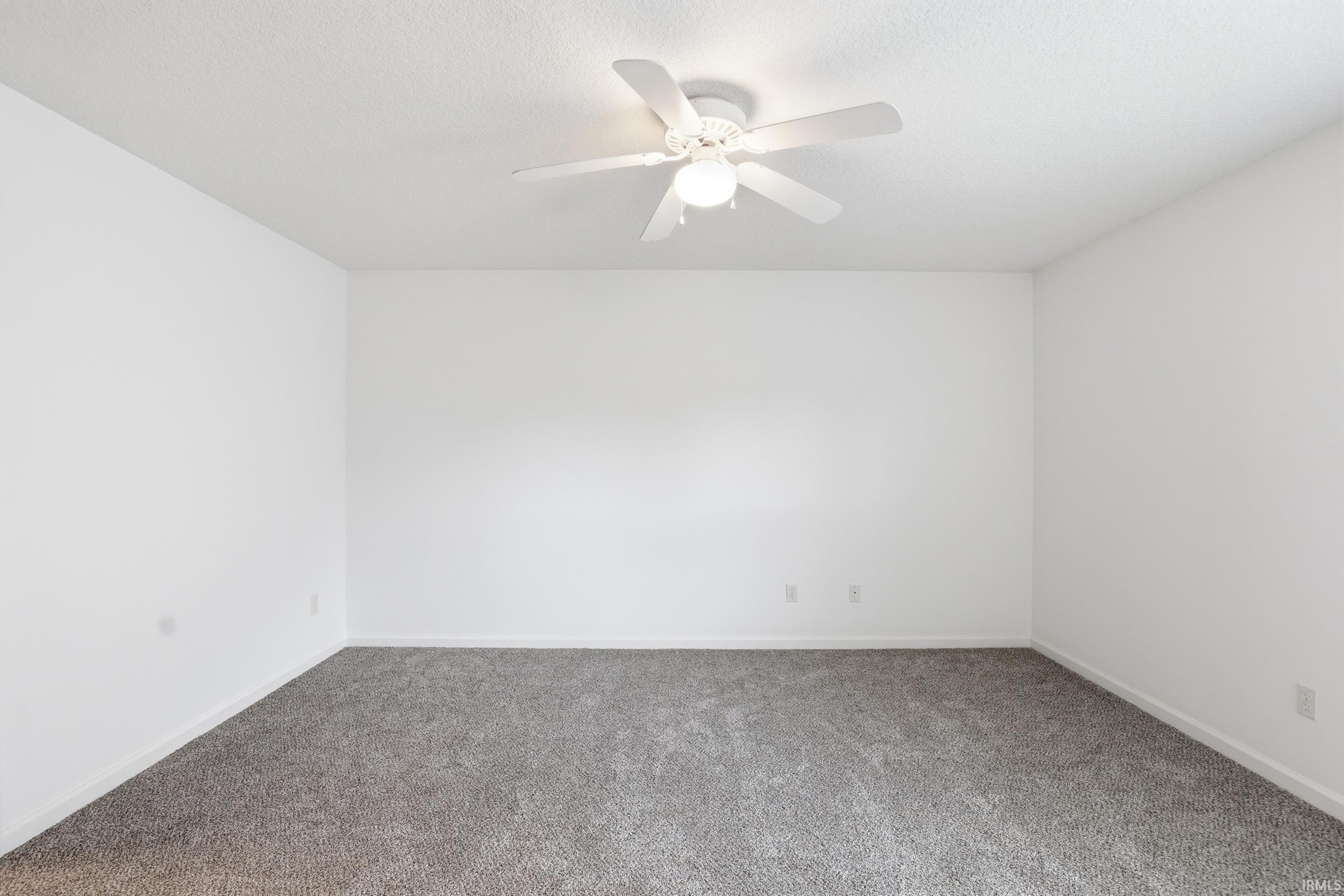 Spacious room featuring neutral carpeting, white walls, and a ceiling fan with integrated lighting