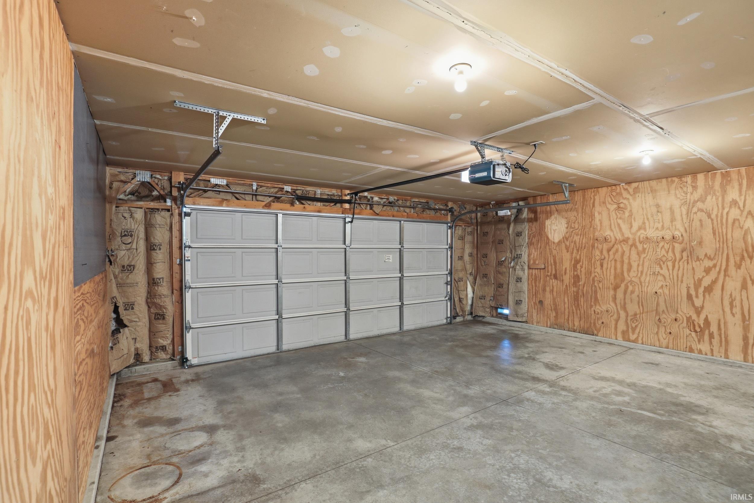 Spacious garage featuring a concrete floor, plywood walls, and a multi-panel overhead door with an automatic opener