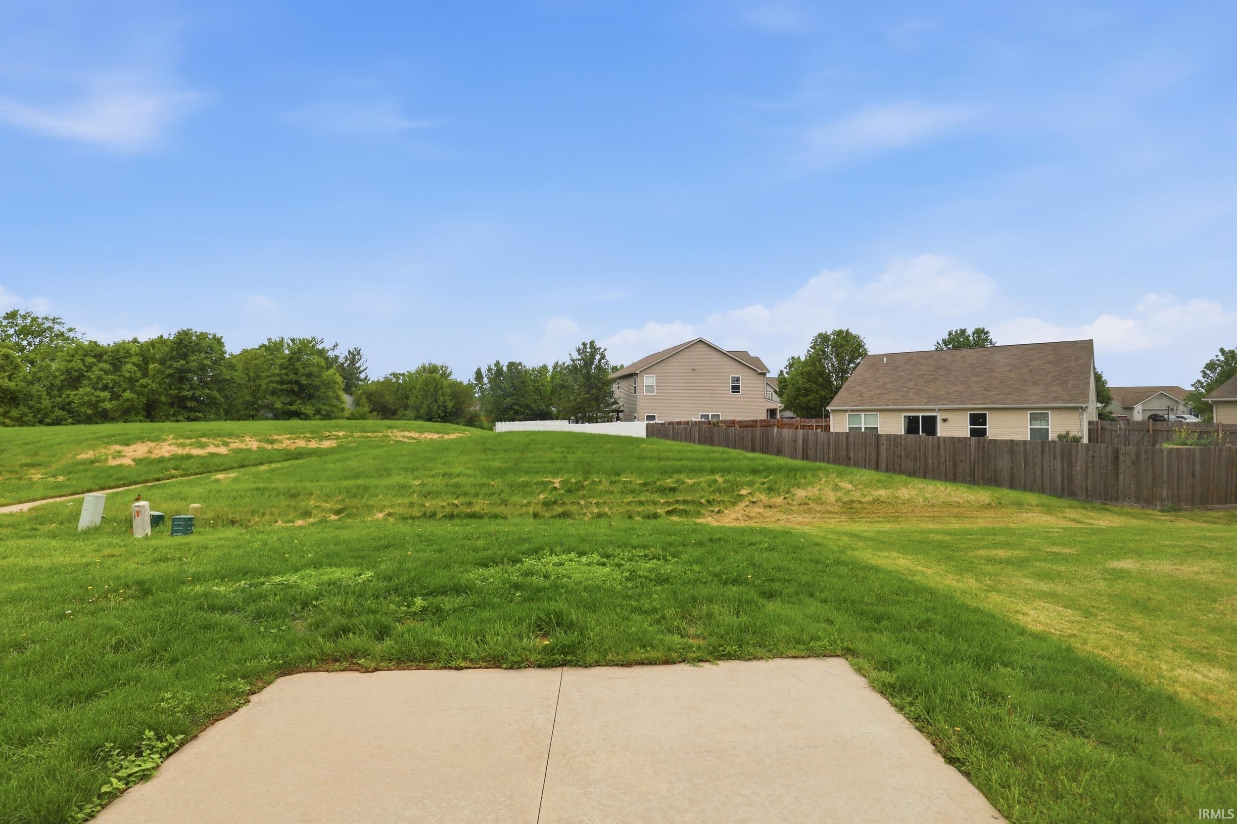 Concrete patio with extensive green lawn, bordered by a wood fence