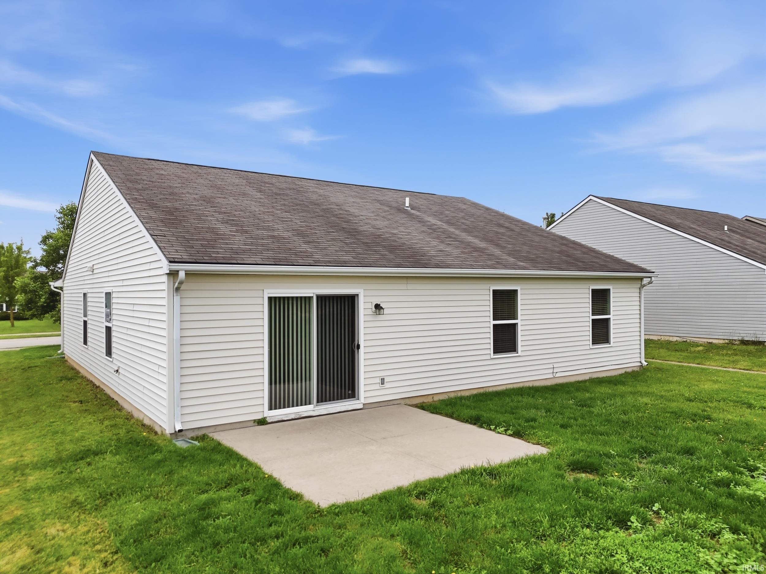 Rear exterior featuring white horizontal siding, a dark shingle roof, a concrete patio, and a sliding glass door