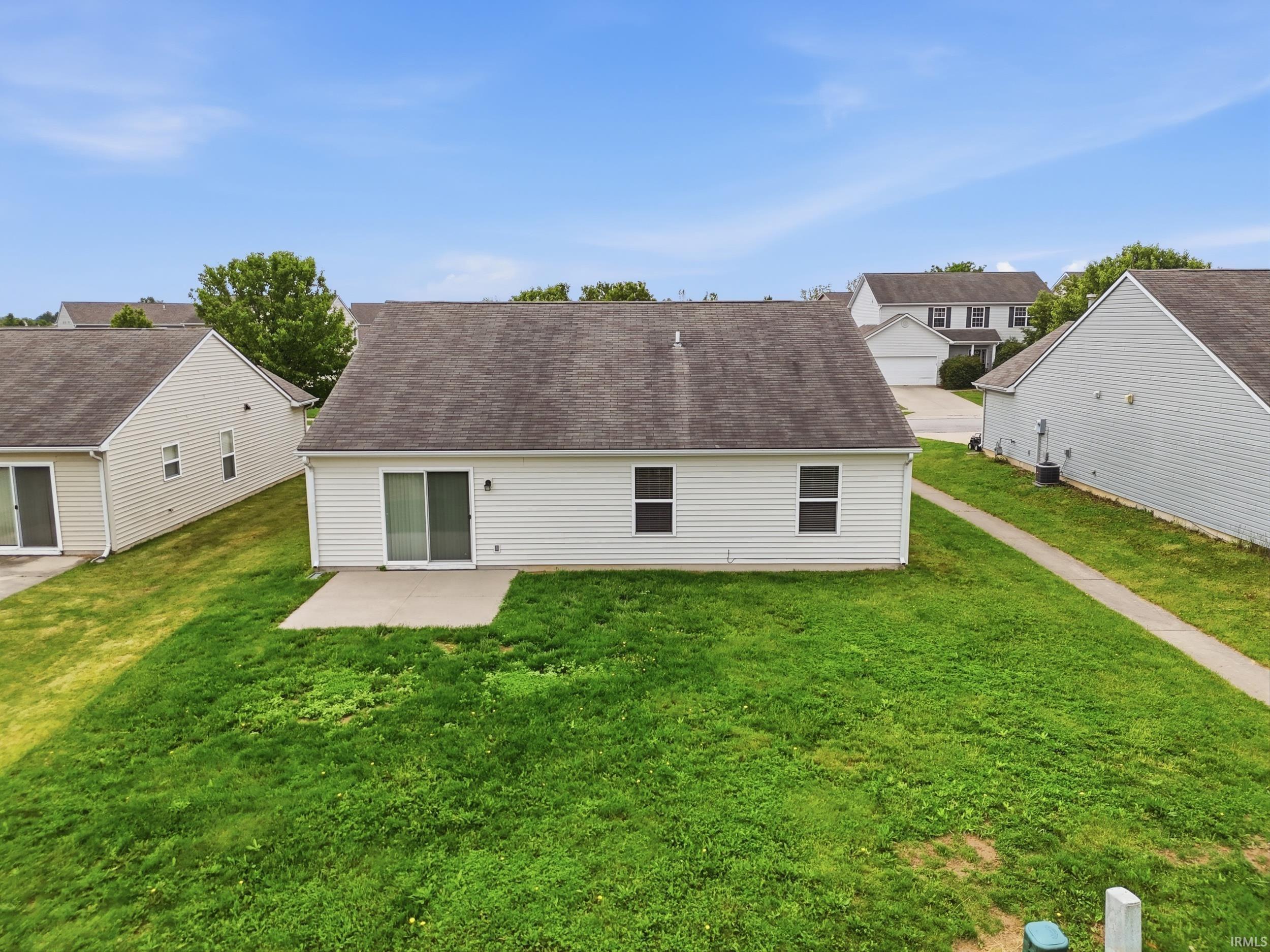 Rear exterior featuring white vinyl siding, a dark shingle roof, and a concrete patio