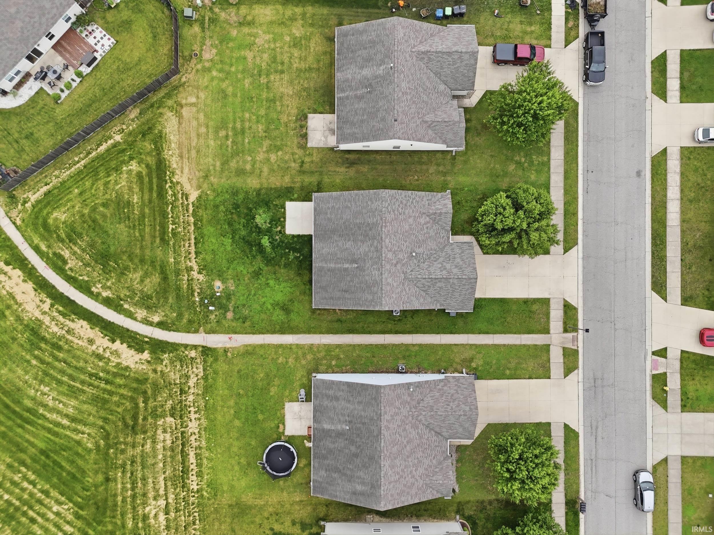 Overhead view of a residential street featuring three properties with gray shingle roofs, concrete driveways, and green lawns