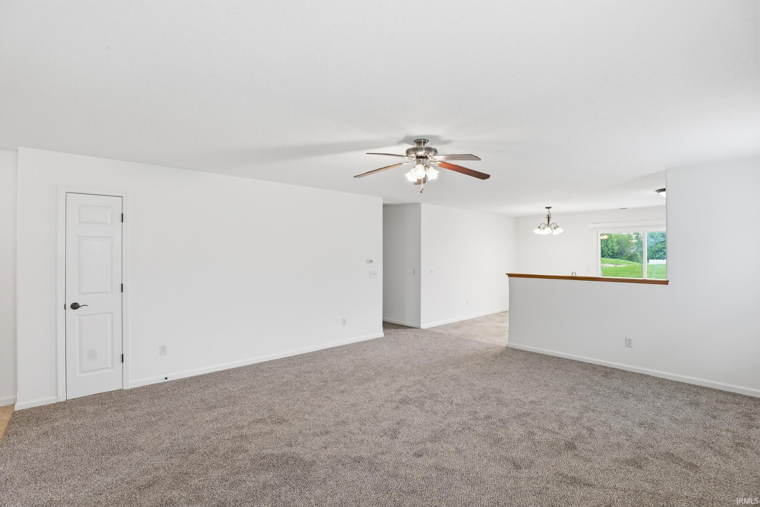 Expansive carpeted area with white walls and a ceiling fan