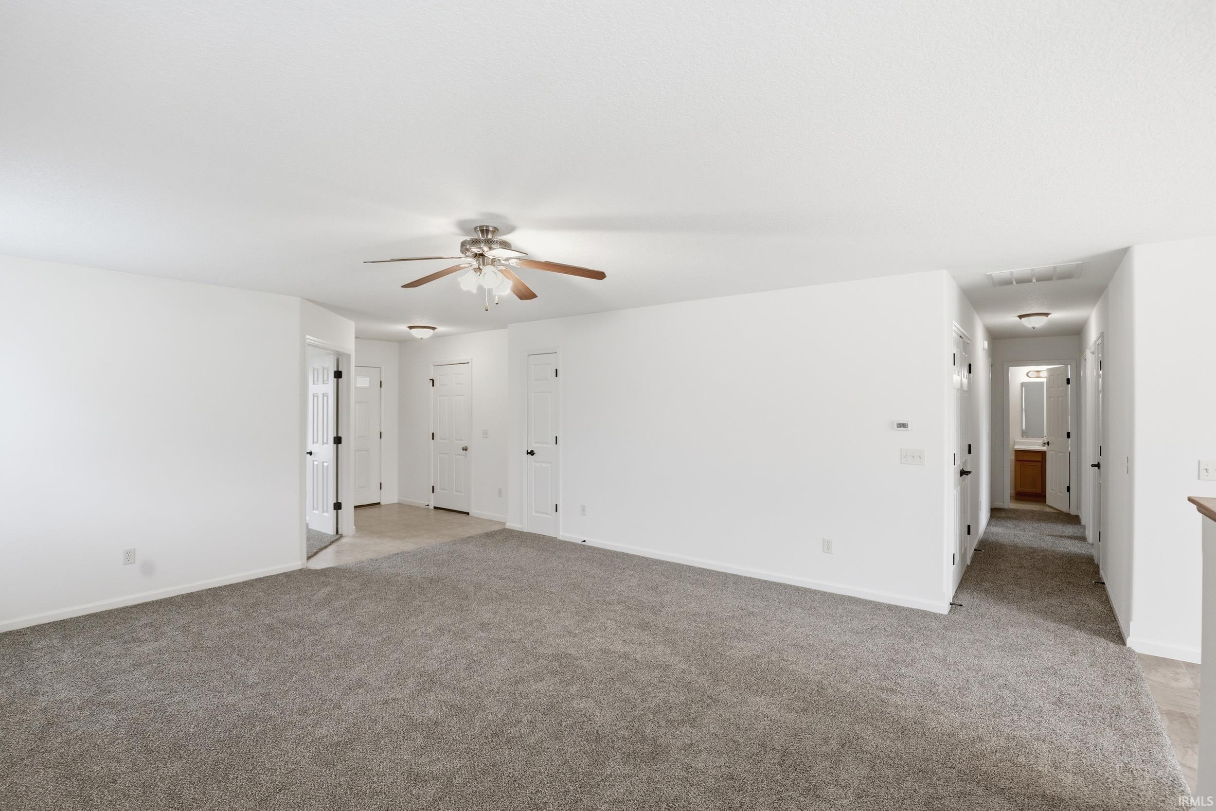 Spacious room featuring neutral carpeting, white walls, a ceiling fan with integrated lighting, and multiple white paneled doors leading to other areas