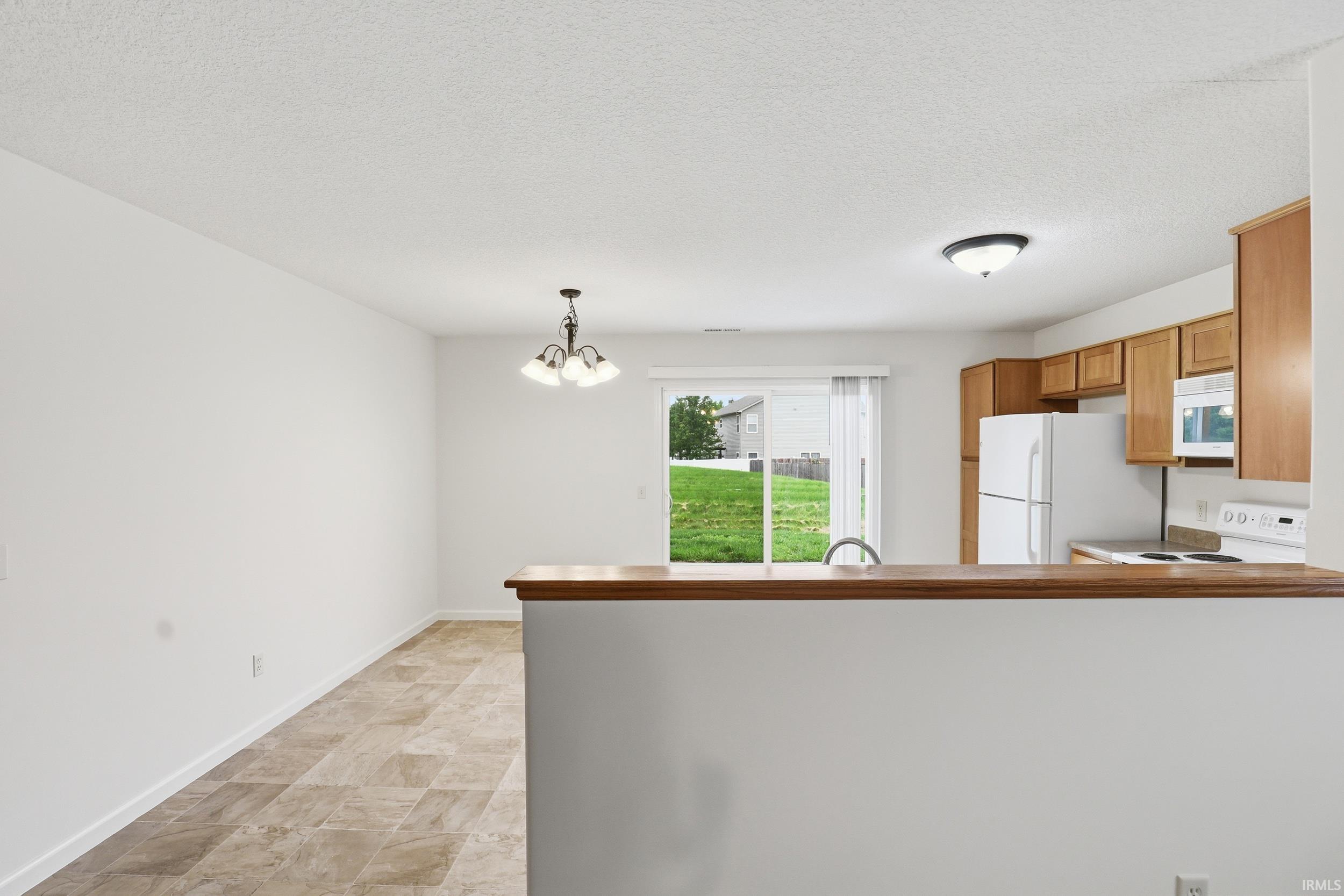 Open concept living space featuring a breakfast bar with a wood-finish countertop, a kitchen with wood-finish cabinetry and white appliances, and tiled flooring